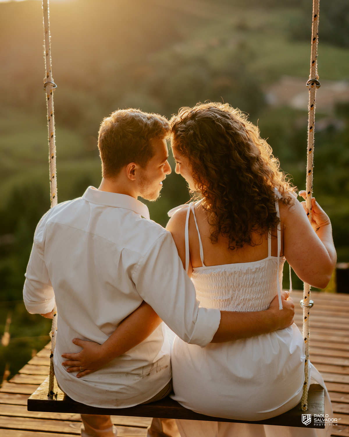 Casal em balanço com vista para montanhas em ensaio pré-wedding em Rio dos Cedros, pôr do sol dourado e paisagem natural, referência para ensaios na Barragem Rio Bonito, Palmeiras e Região dos Lagos.