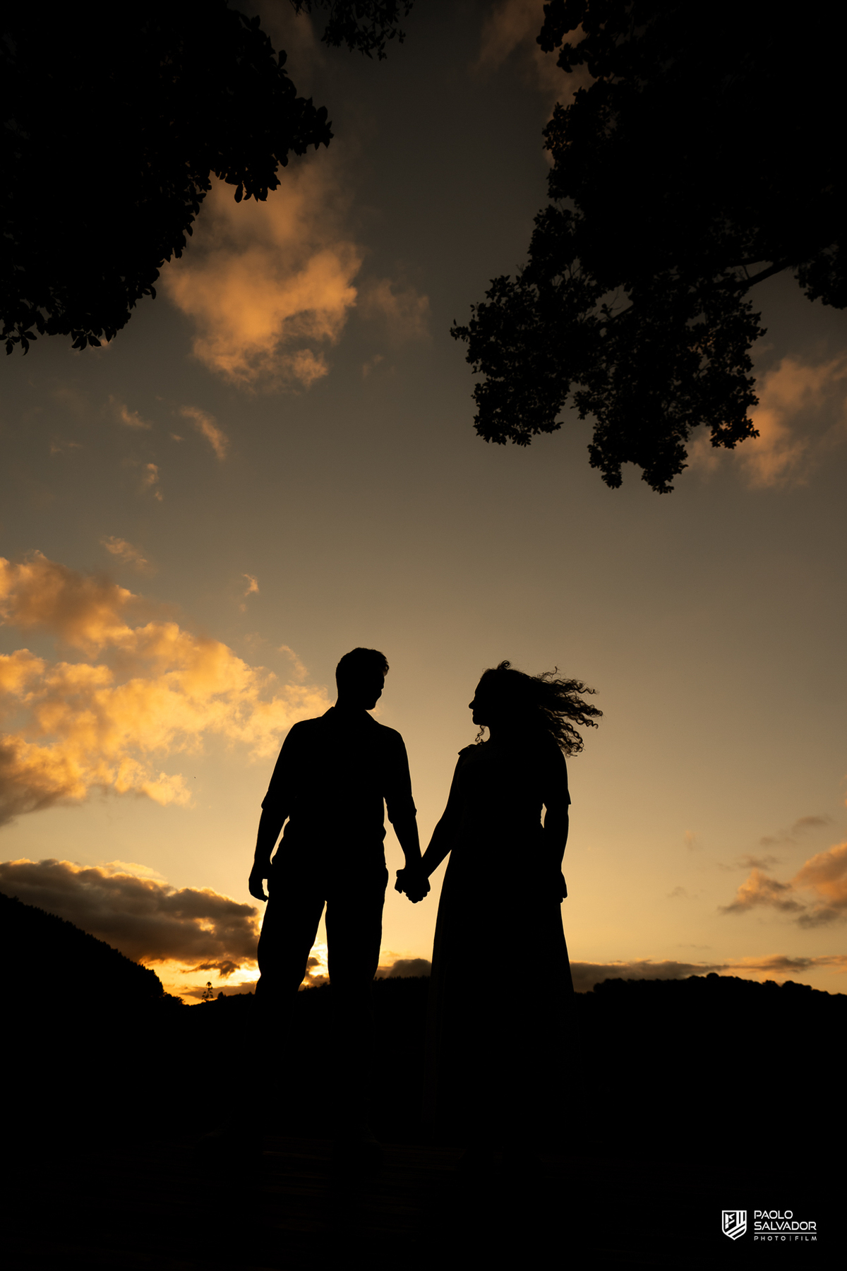 Silhueta de casal ao pôr do sol em ensaio pré-wedding em Rio dos Cedros, com céu dramático e estética cinematográfica, ideal para quem busca ensaios nas barragens e Altos Cedros.
