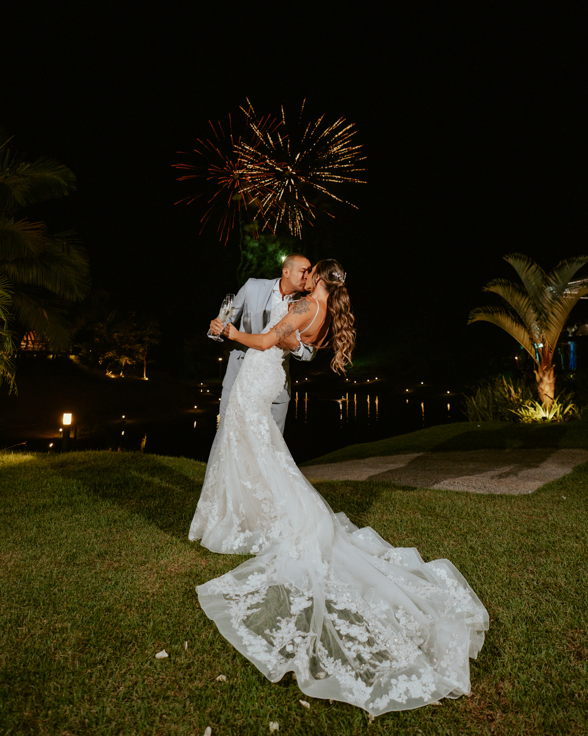 Noivos brindando com espumante durante festa de casamento com fogos ao fundo no Refúgio dos Lagos em Massaranduba, momento marcante e celebração.