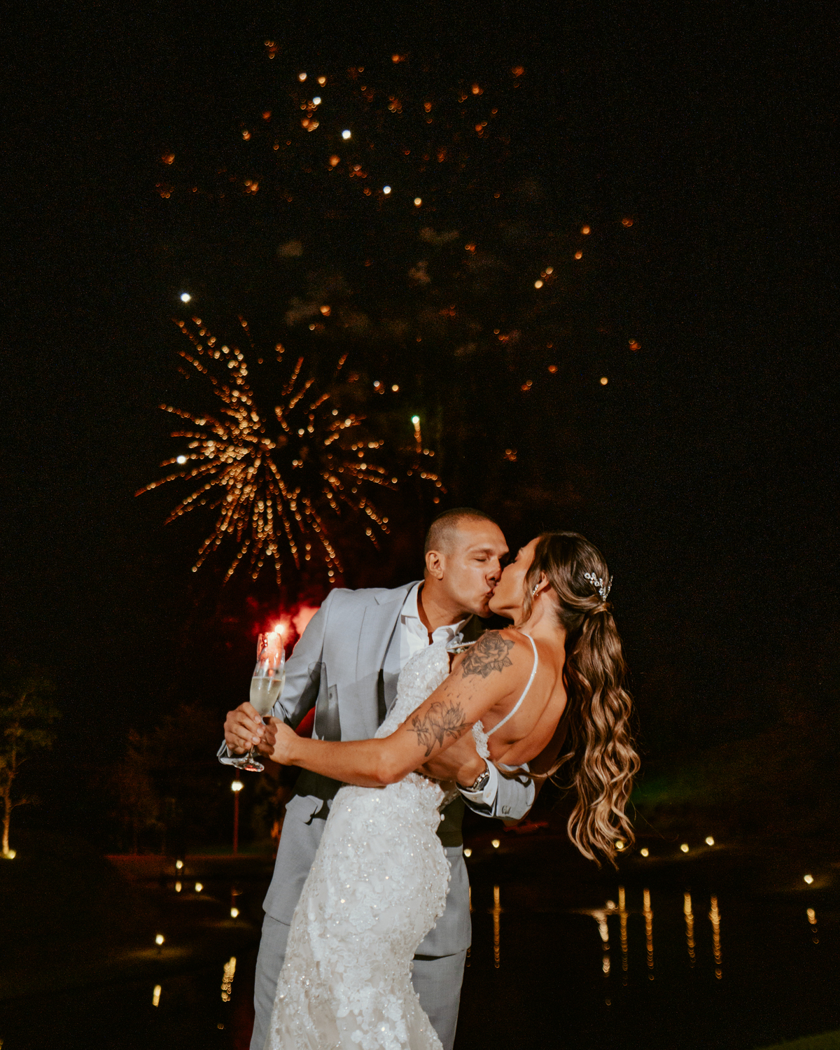 Noivos brindando com espumante durante festa de casamento com fogos ao fundo no Refúgio dos Lagos em Massaranduba, momento marcante e celebração.