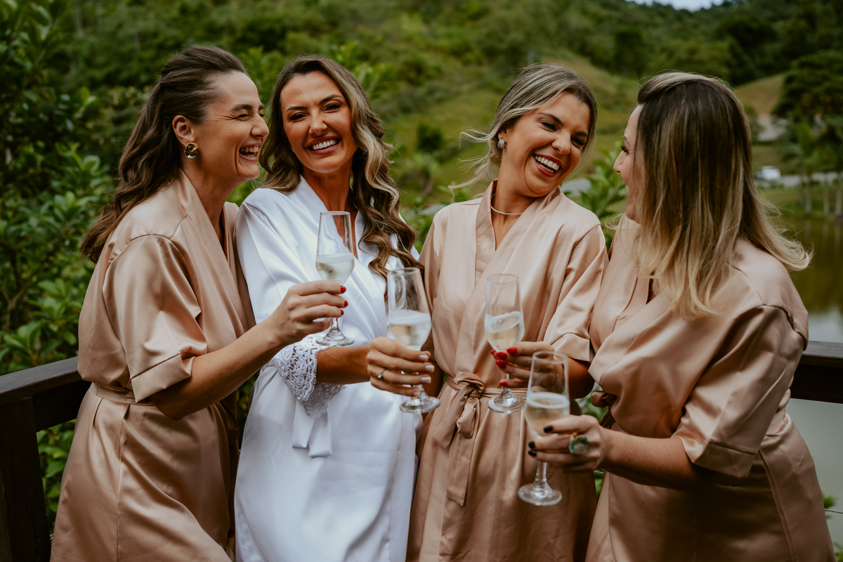 Noiva brindando com madrinhas no chalé do Refúgio dos Lagos em Massaranduba, momento descontraído e elegante antes da cerimônia, inspiração para casamentos em Joinville, Jaraguá e região.
