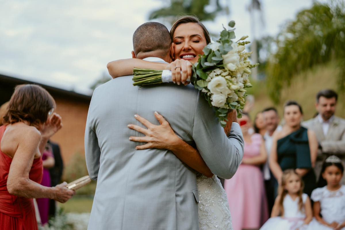 Noiva entrando na cerimônia acompanhada de familiares em casamento ao ar livre no Refúgio dos Lagos em Massaranduba, com convidados emocionados e cenário natural.
