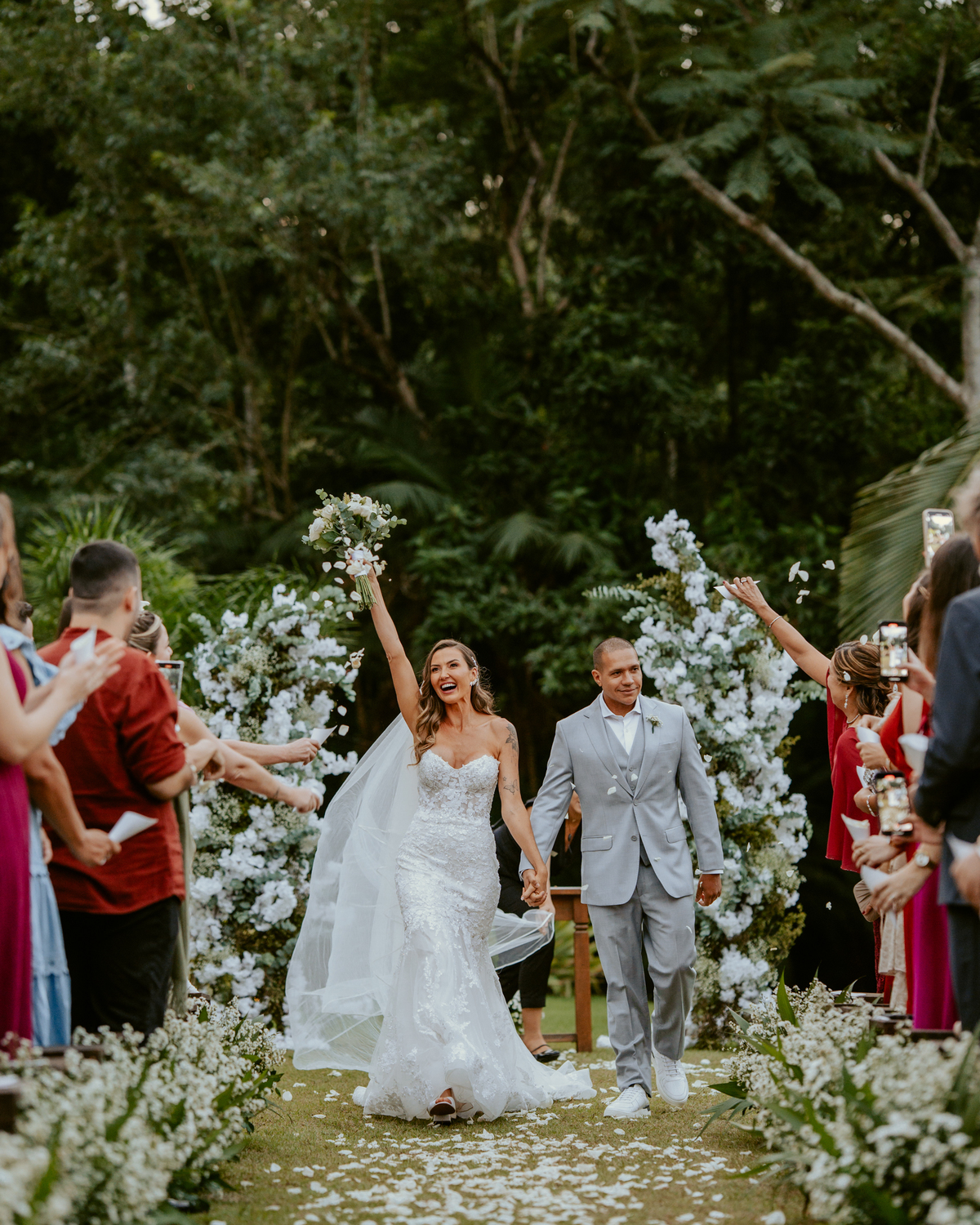 Saída dos noivos após cerimônia de casamento em Massaranduba no Refúgio dos Lagos com pétalas e celebração dos convidados.