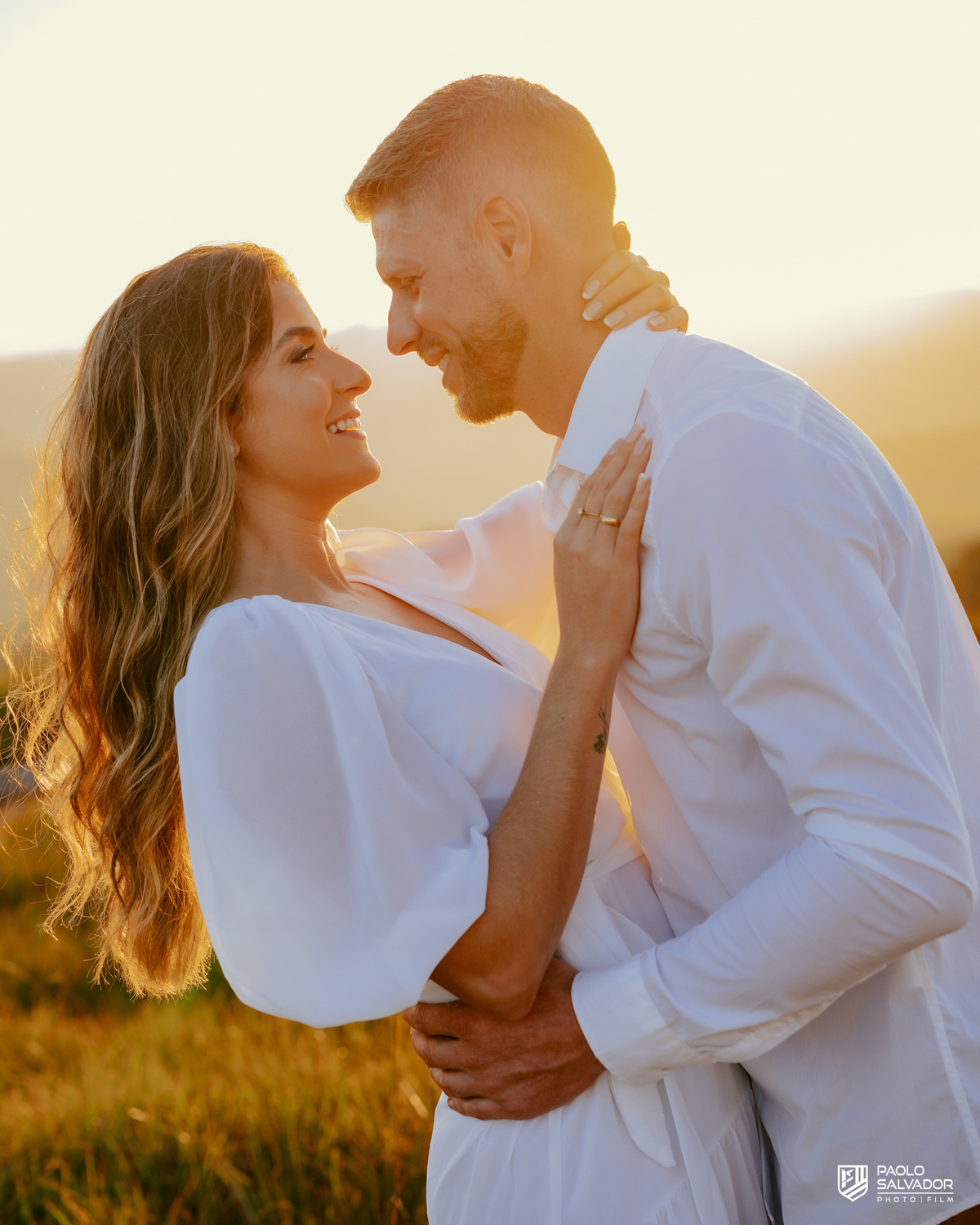 Casal sorrindo e caminhando em meio ao campo durante ensaio pré-wedding na Serra Catarinense, com vento, movimento e luz de fim de tarde.