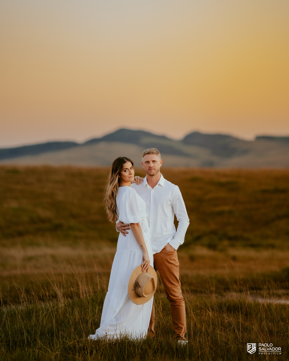 Casal caminhando de mãos dadas em campo aberto durante ensaio pré-wedding em Rancho Queimado, com cenário amplo e estética inspirada na Serra Gaúcha.