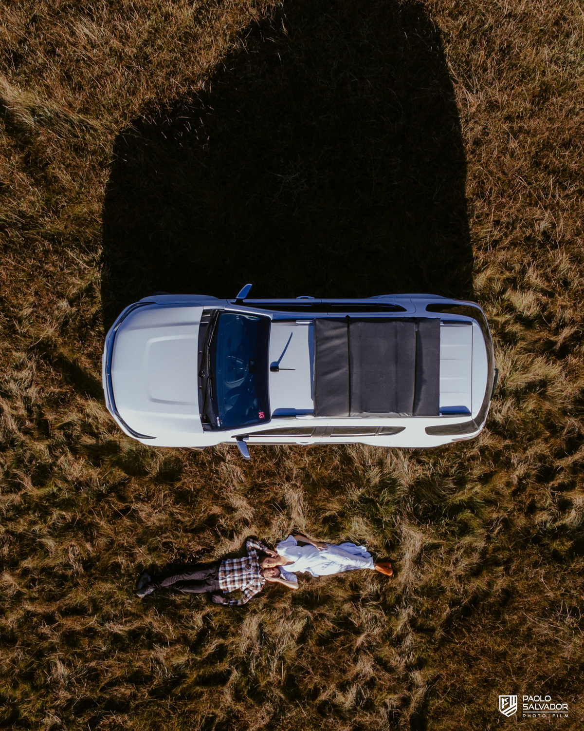 Casal Tainá e Leandro abraçados em frente à caminhonete Trailblazer durante ensaio pré-wedding em Rancho Queimado, com luz dourada e paisagem de campo típica da Serra Catarinense.