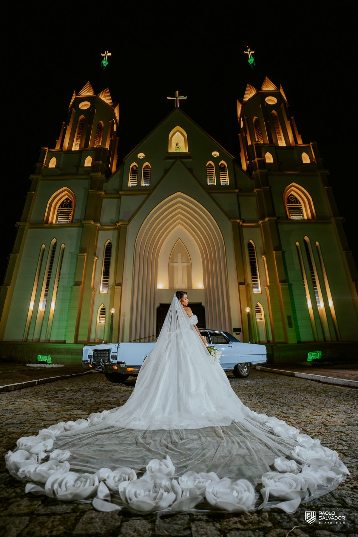 Retrato do casal com carro clássico na frente da Igreja Santa Inês em Indaial à noite, fotografia elegante e romântica de casamento SC