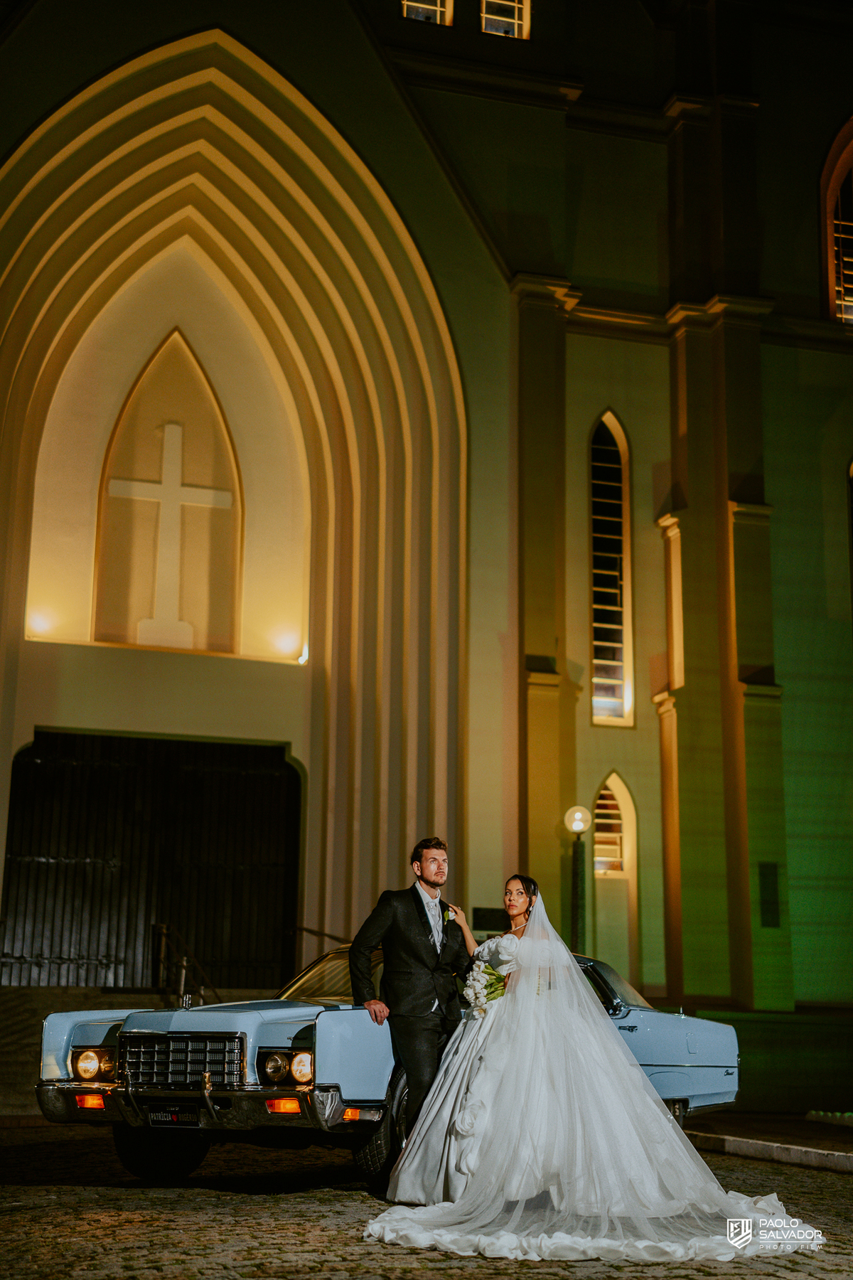 Retrato do casal com carro clássico na frente da Igreja Santa Inês em Indaial à noite, fotografia elegante e romântica de casamento SC