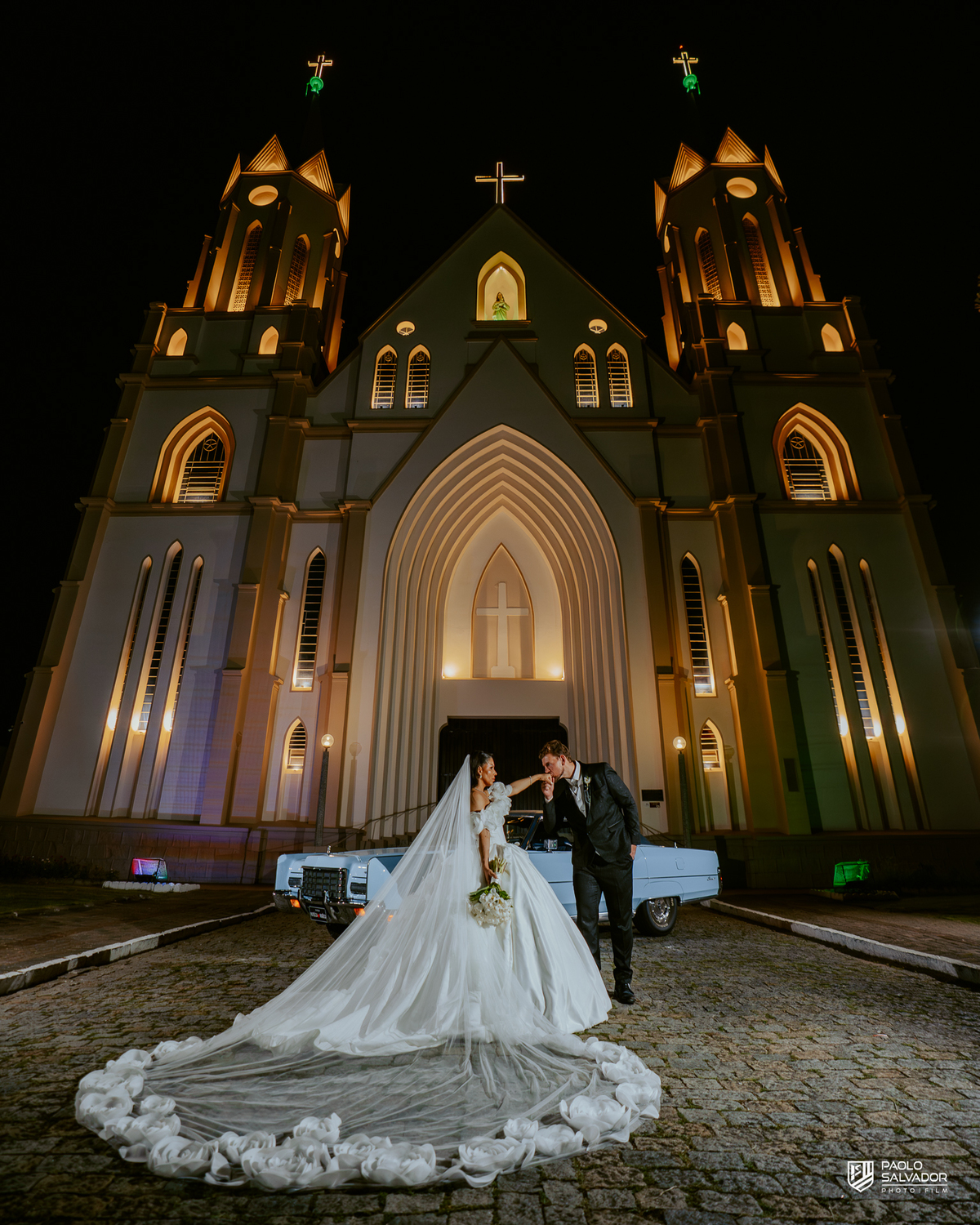 Retrato do casal com carro clássico na frente da Igreja Santa Inês em Indaial à noite, fotografia elegante e romântica de casamento SC