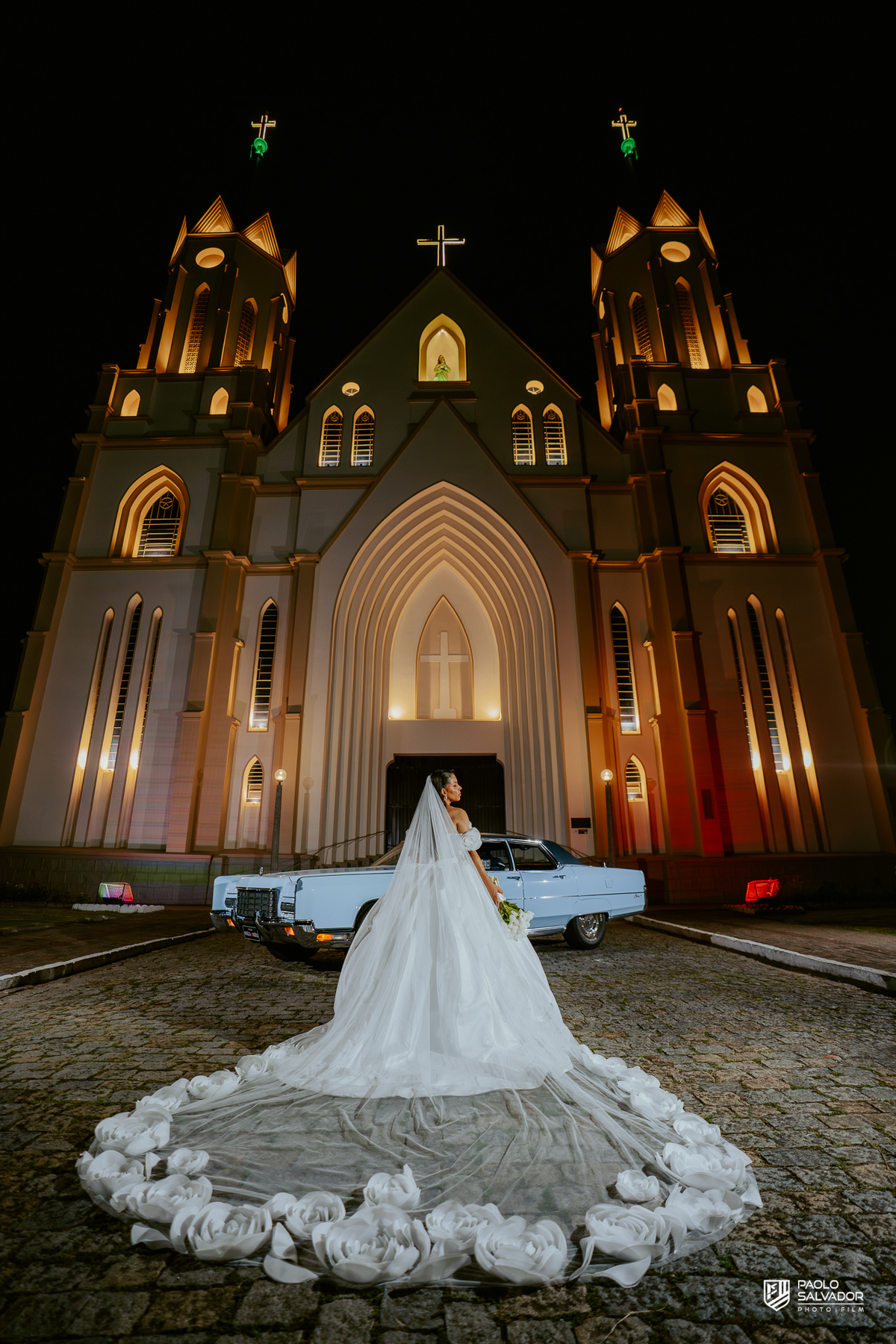 Retrato do casal com carro clássico na frente da Igreja Santa Inês em Indaial à noite, fotografia elegante e romântica de casamento SC