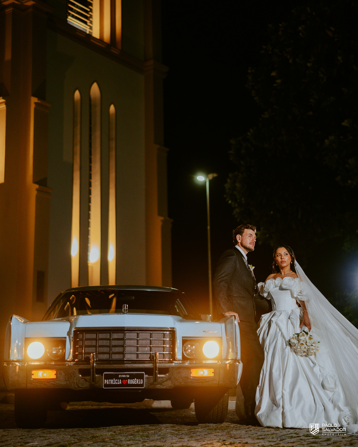 Retrato do casal com carro clássico na frente da Igreja Santa Inês em Indaial à noite, fotografia elegante e romântica de casamento SC