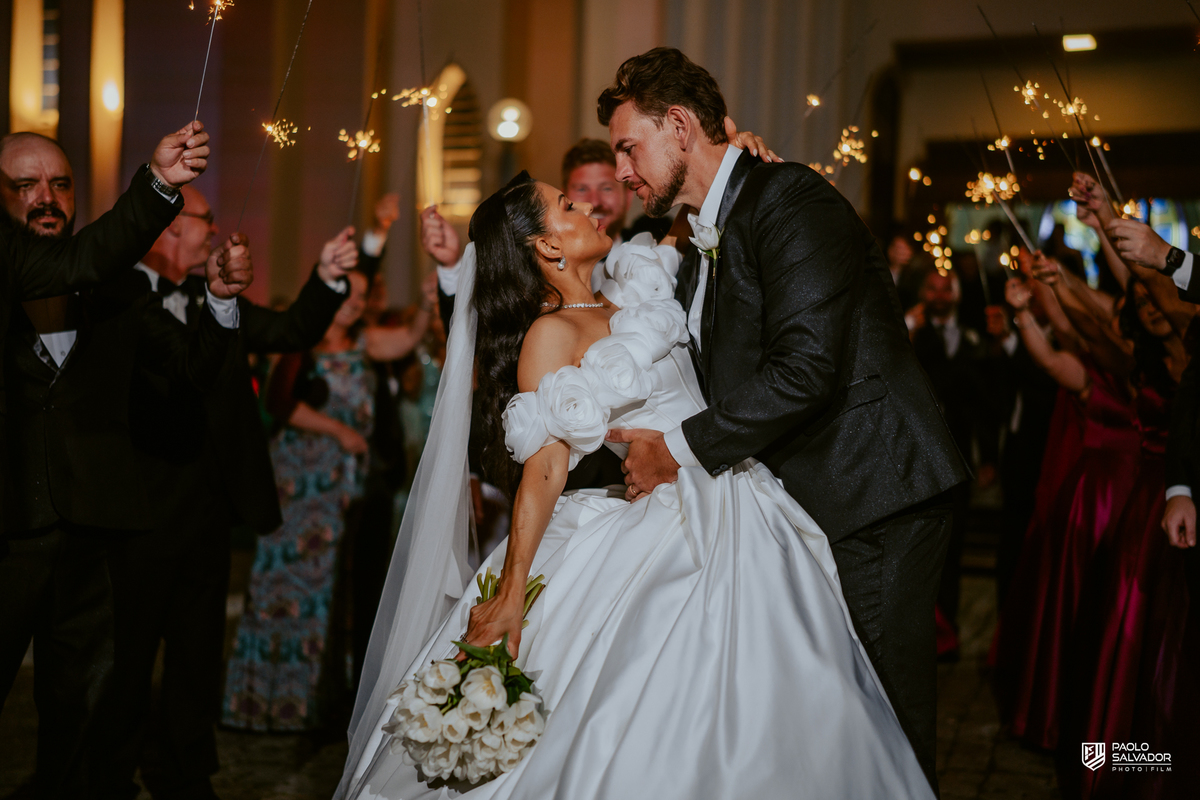 Saída dos noivos com sparkles em frente à Igreja Santa Inês em Indaial, beijo do casal, fotografia de casamento noturno cinematográfico
