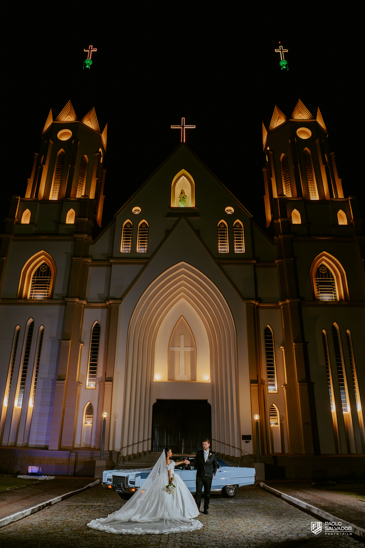 Retrato do casal com carro clássico na frente da Igreja Santa Inês em Indaial à noite, fotografia elegante e romântica de casamento SC
