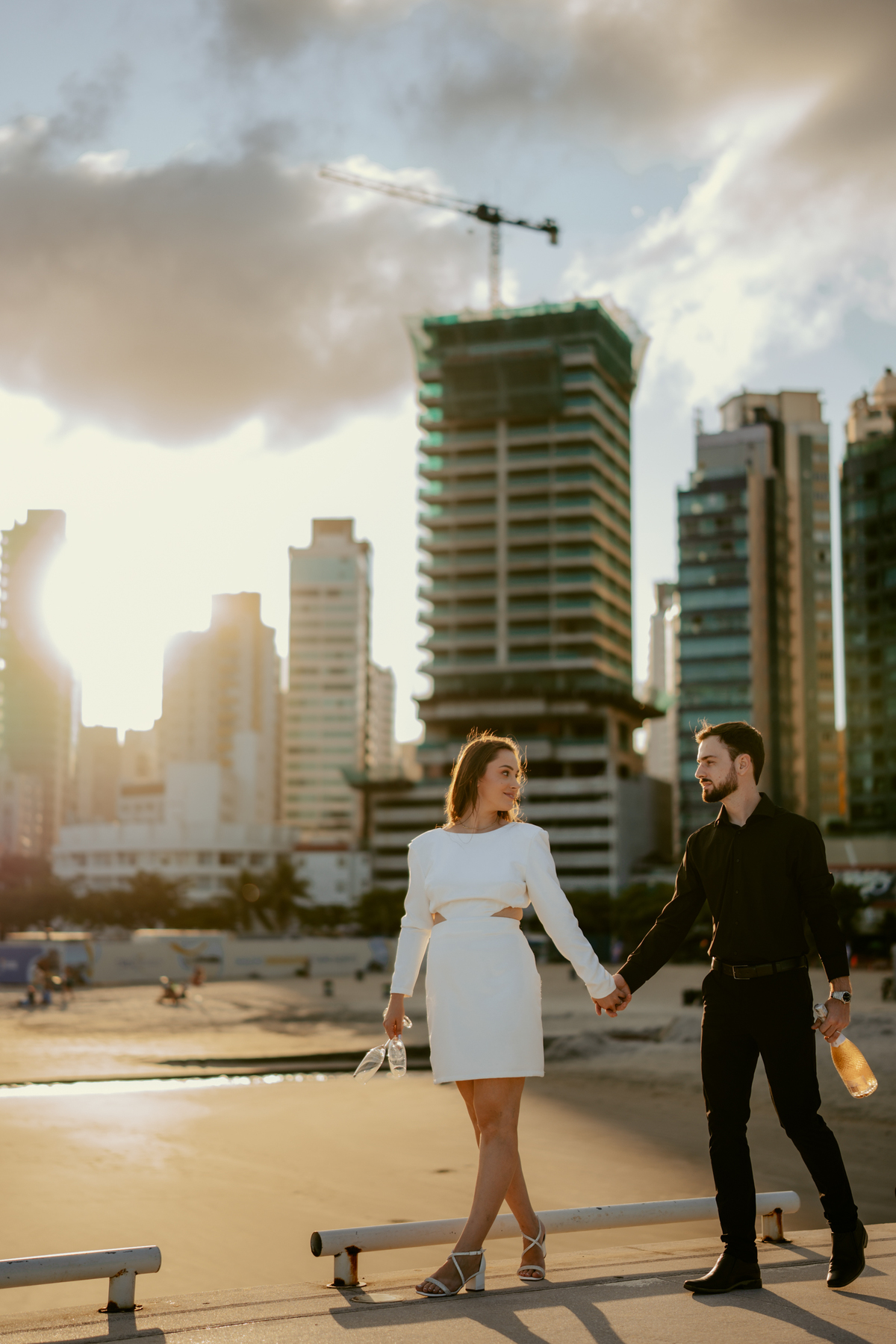 Casal em ensaio pré-wedding na roda gigante FG Big Wheel em Balneário Camboriú, fotos na orla e pier com vista para o mar e prédios, estilo moderno e romântico com luz de pôr do sol e atmosfera urbana sofisticada