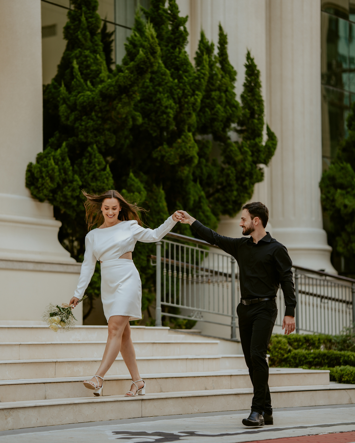 Ensaio pré-wedding na orla de Balneário Camboriú com pôr do sol entre prédios, casal sorrindo com champagne, estilo moderno e divertido, fotografia romântica com luz dourada e cenário urbano contemporâneo