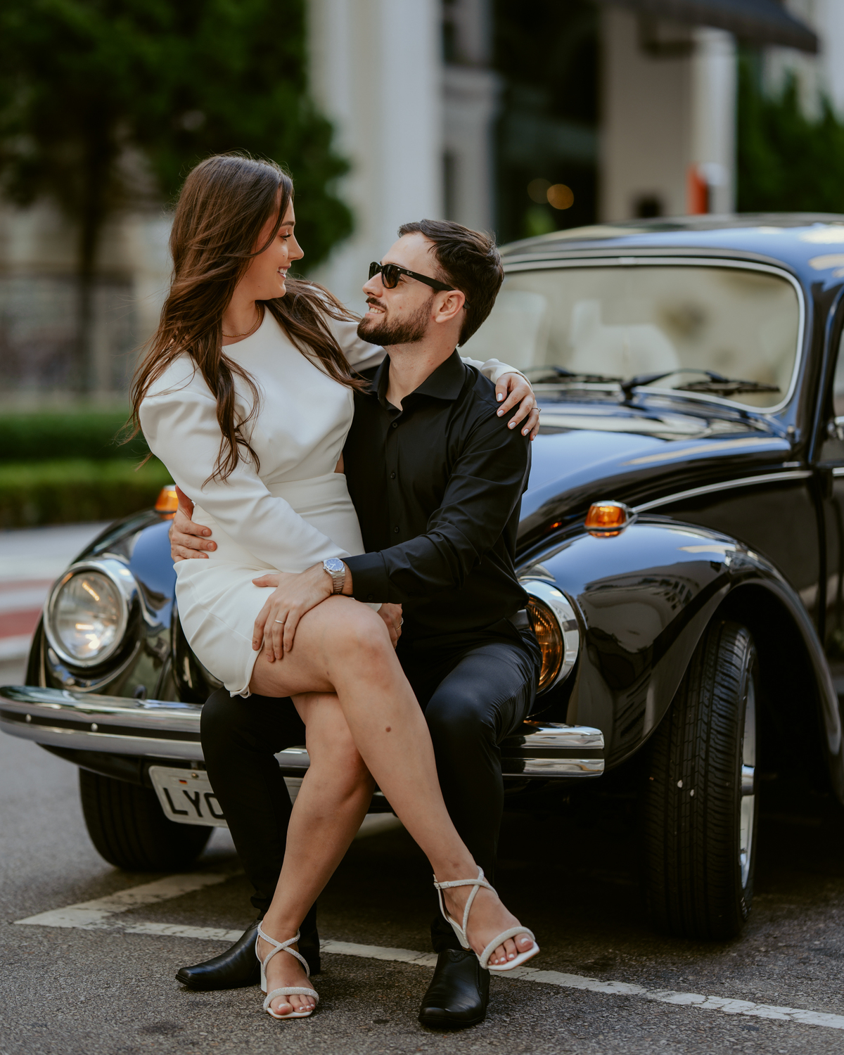 Casal apaixonado em ensaio pré-wedding com arquitetura clássica ao fundo em Balneário Camboriú, composição elegante, roupas sofisticadas preto e branco, fotografia emocional e moderna para casamento