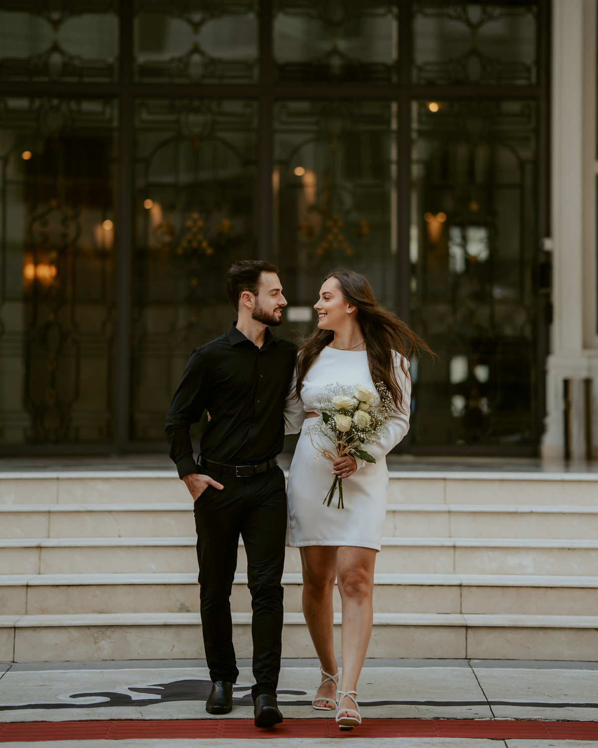 Ensaio pré-wedding na orla de Balneário Camboriú com pôr do sol entre prédios, casal sorrindo com champagne, estilo moderno e divertido, fotografia romântica com luz dourada e cenário urbano contemporâneo