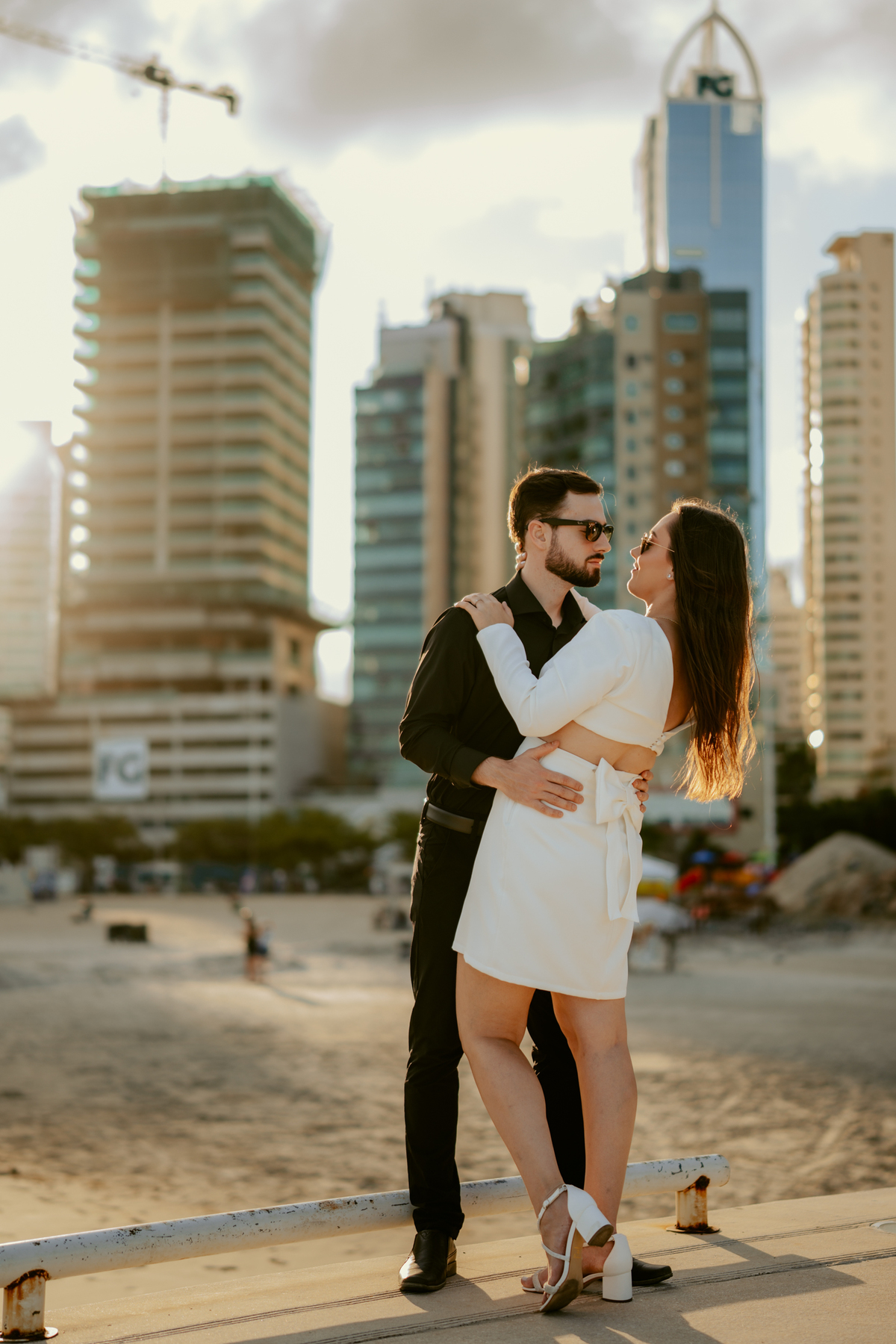 Ensaio pré-wedding de Gabi e Henrique na FG Big Wheel roda gigante de Balneário Camboriú, casal caminhando no pier da orla ao pôr do sol, fotografia urbana romântica com skyline ao fundo e luz dourada cinematográfica