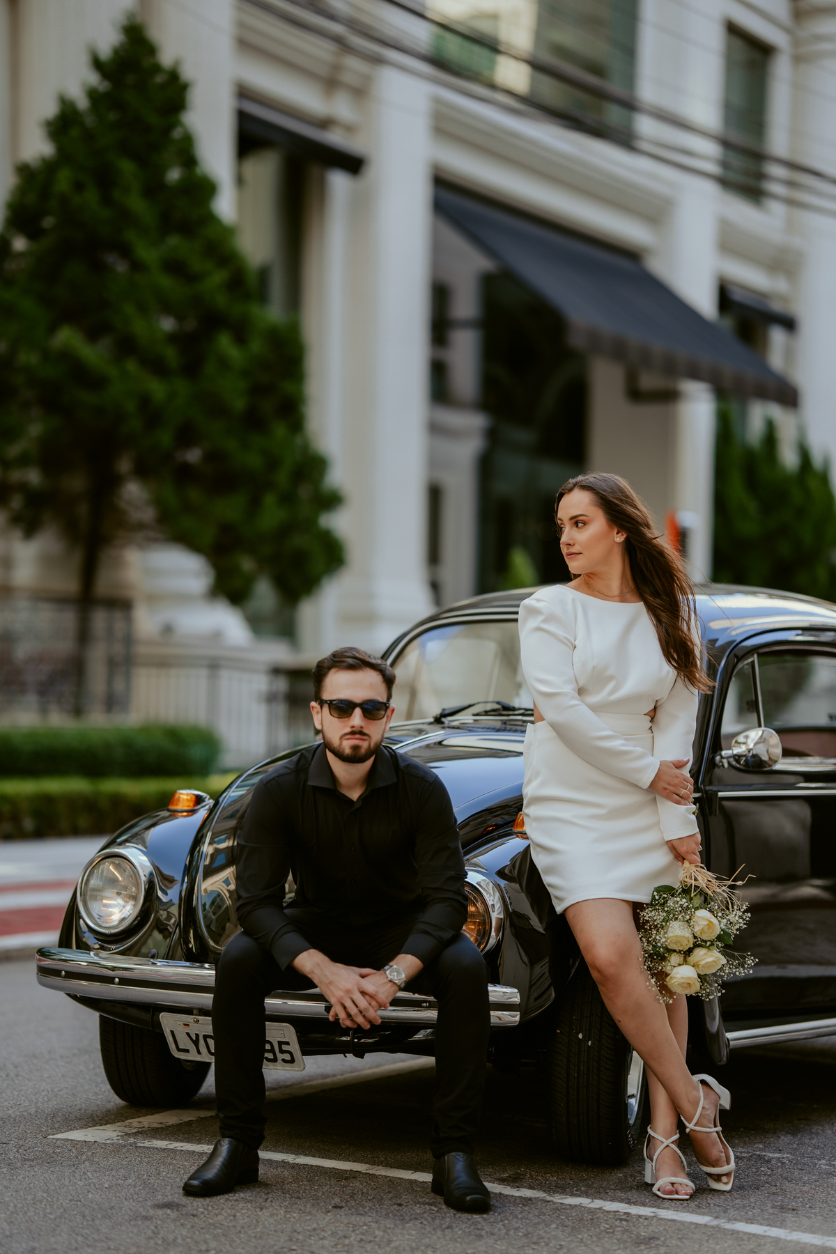 Casal apaixonado em ensaio pré-wedding com arquitetura clássica ao fundo em Balneário Camboriú, composição elegante, roupas sofisticadas preto e branco, fotografia emocional e moderna para casamento