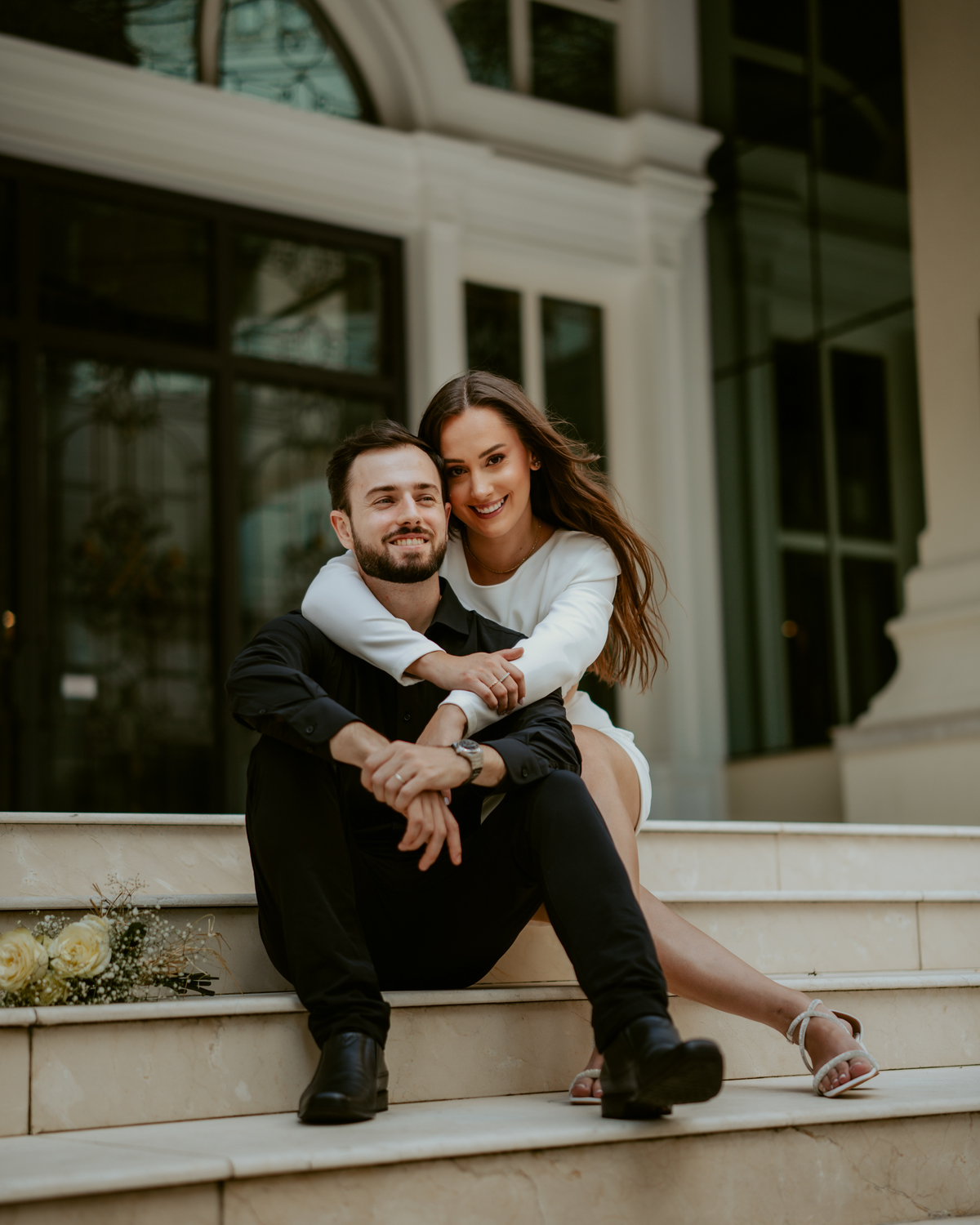 Ensaio pré-wedding ao pôr do sol na praia de Balneário Camboriú com skyline urbano ao fundo, casal brindando com champagne, estilo contemporâneo, romântico e espontâneo, fotografia profissional de casamento