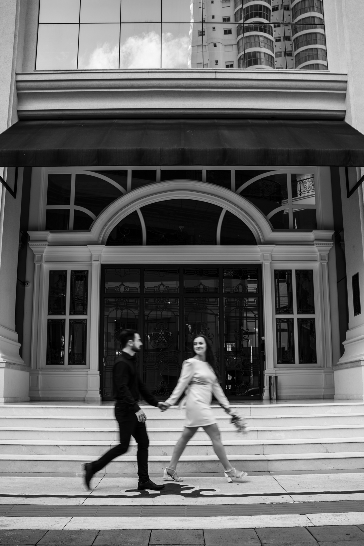 Ensaio pré-wedding ao pôr do sol na praia de Balneário Camboriú com skyline urbano ao fundo, casal brindando com champagne, estilo contemporâneo, romântico e espontâneo, fotografia profissional de casamento