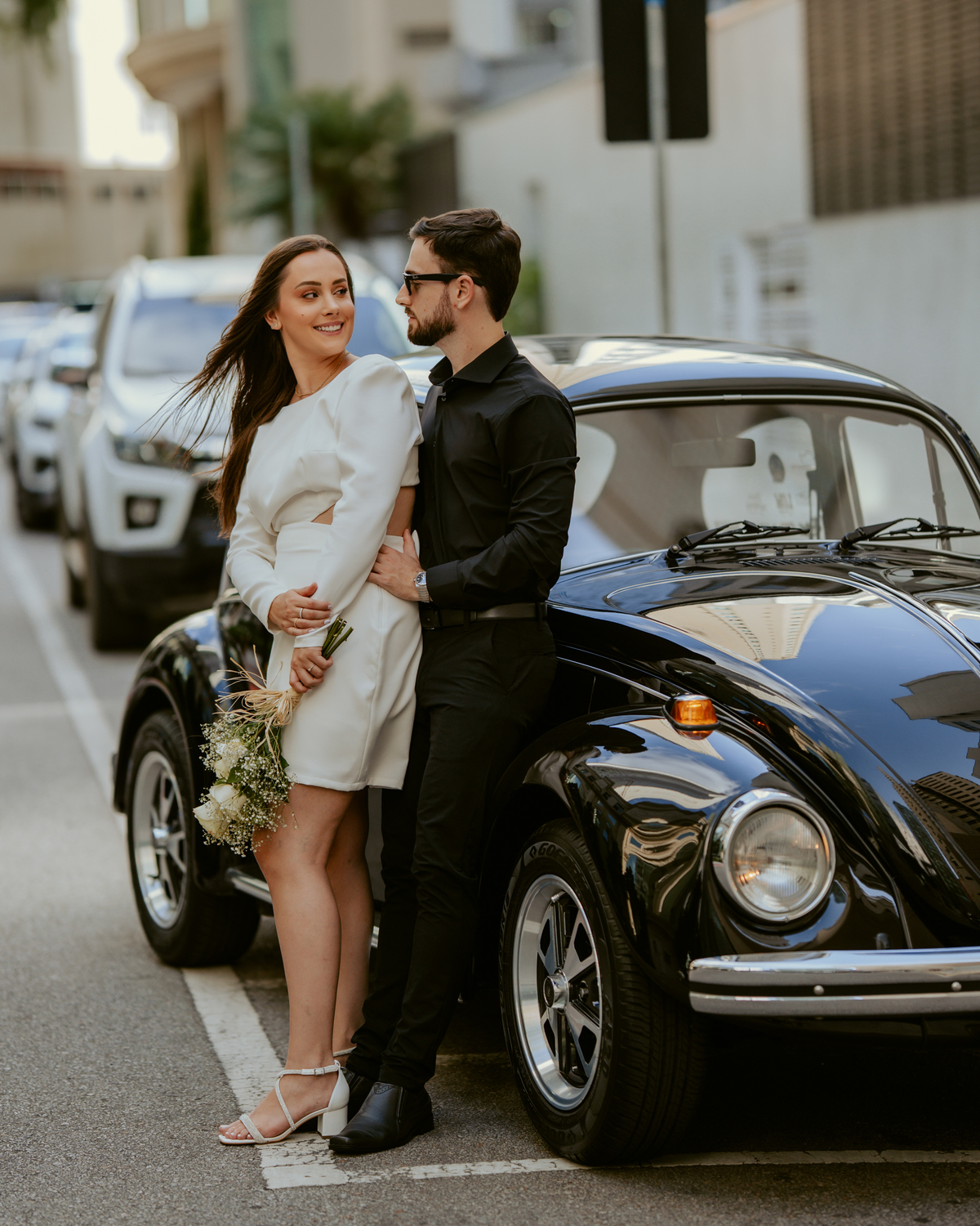 Ensaio pré-wedding ao pôr do sol na praia de Balneário Camboriú com skyline urbano ao fundo, casal brindando com champagne, estilo contemporâneo, romântico e espontâneo, fotografia profissional de casamento