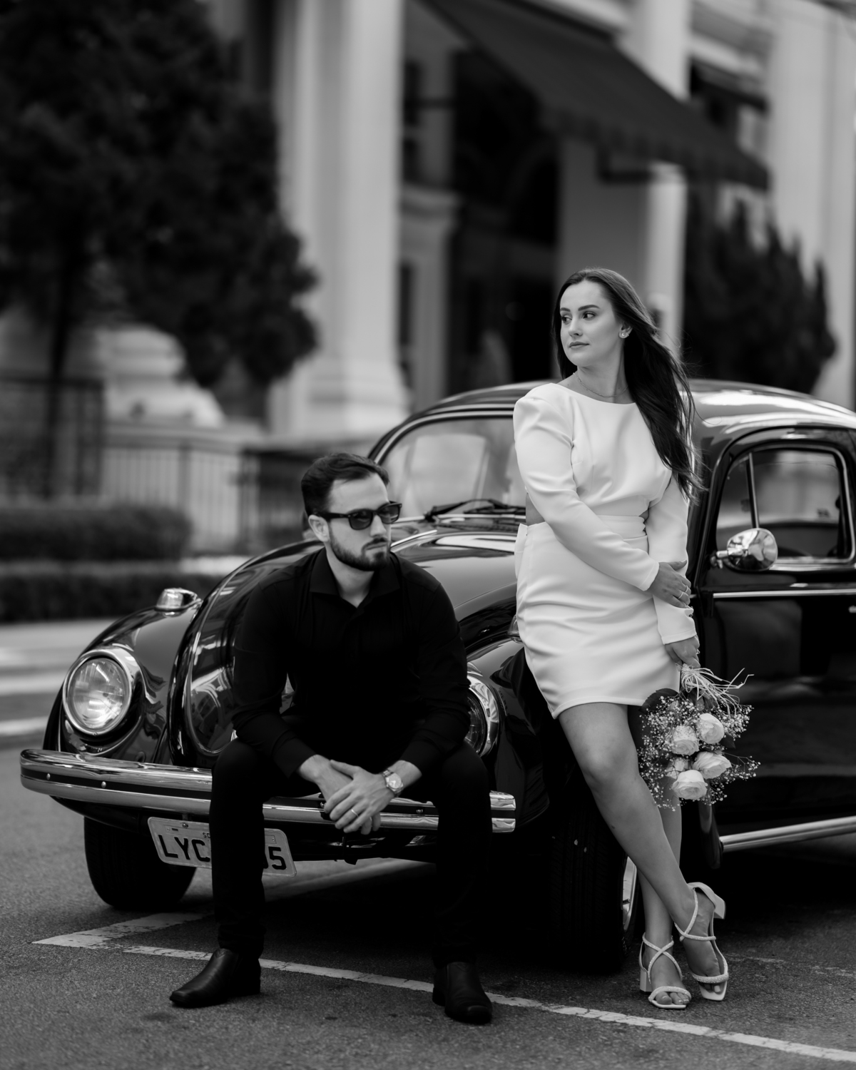 Casal apaixonado em ensaio pré-wedding com arquitetura clássica ao fundo em Balneário Camboriú, composição elegante, roupas sofisticadas preto e branco, fotografia emocional e moderna para casamento