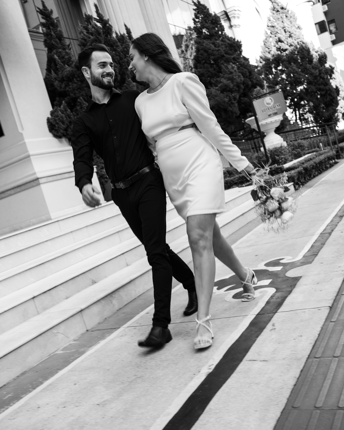 Ensaio pré-wedding ao pôr do sol na praia de Balneário Camboriú com skyline urbano ao fundo, casal brindando com champagne, estilo contemporâneo, romântico e espontâneo, fotografia profissional de casamento