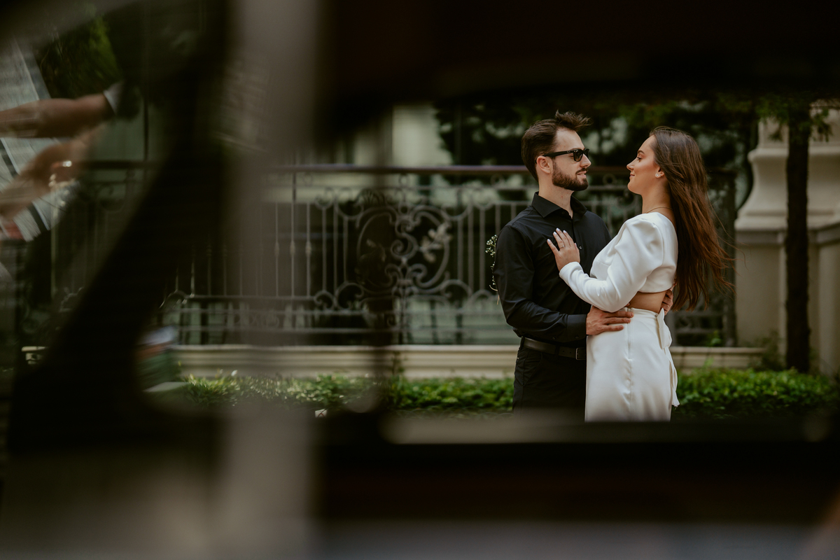 Casal apaixonado em ensaio pré-wedding com arquitetura clássica ao fundo em Balneário Camboriú, composição elegante, roupas sofisticadas preto e branco, fotografia emocional e moderna para casamento