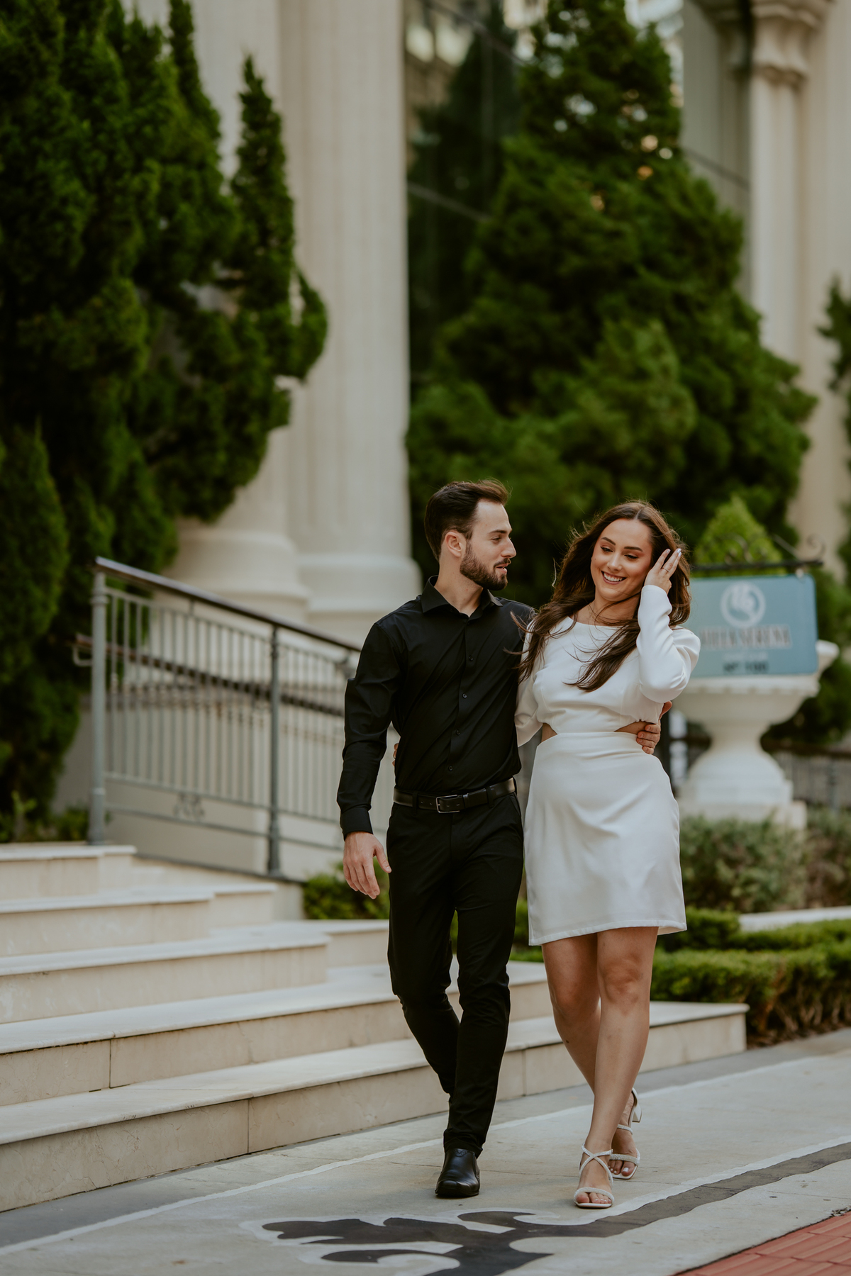 Ensaio pré-wedding na orla de Balneário Camboriú com pôr do sol entre prédios, casal sorrindo com champagne, estilo moderno e divertido, fotografia romântica com luz dourada e cenário urbano contemporâneo