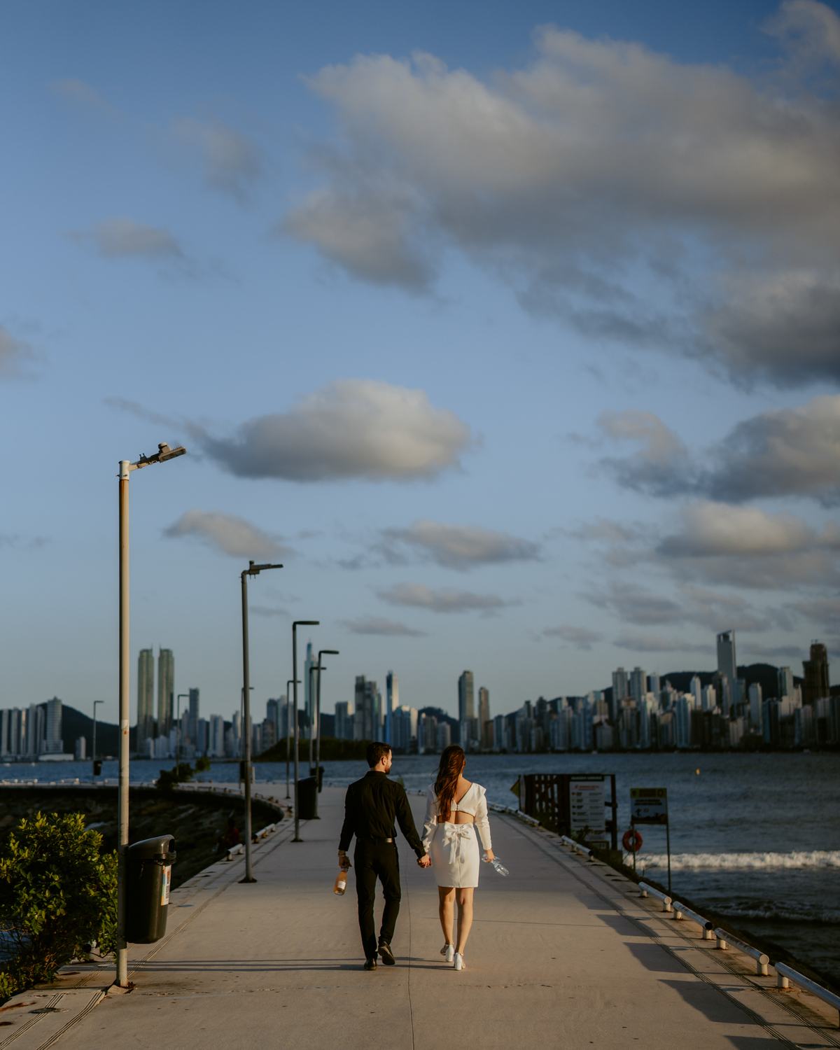 Casal em ensaio pré-wedding na roda gigante FG Big Wheel em Balneário Camboriú, fotos na orla e pier com vista para o mar e prédios, estilo moderno e romântico com luz de pôr do sol e atmosfera urbana sofisticada