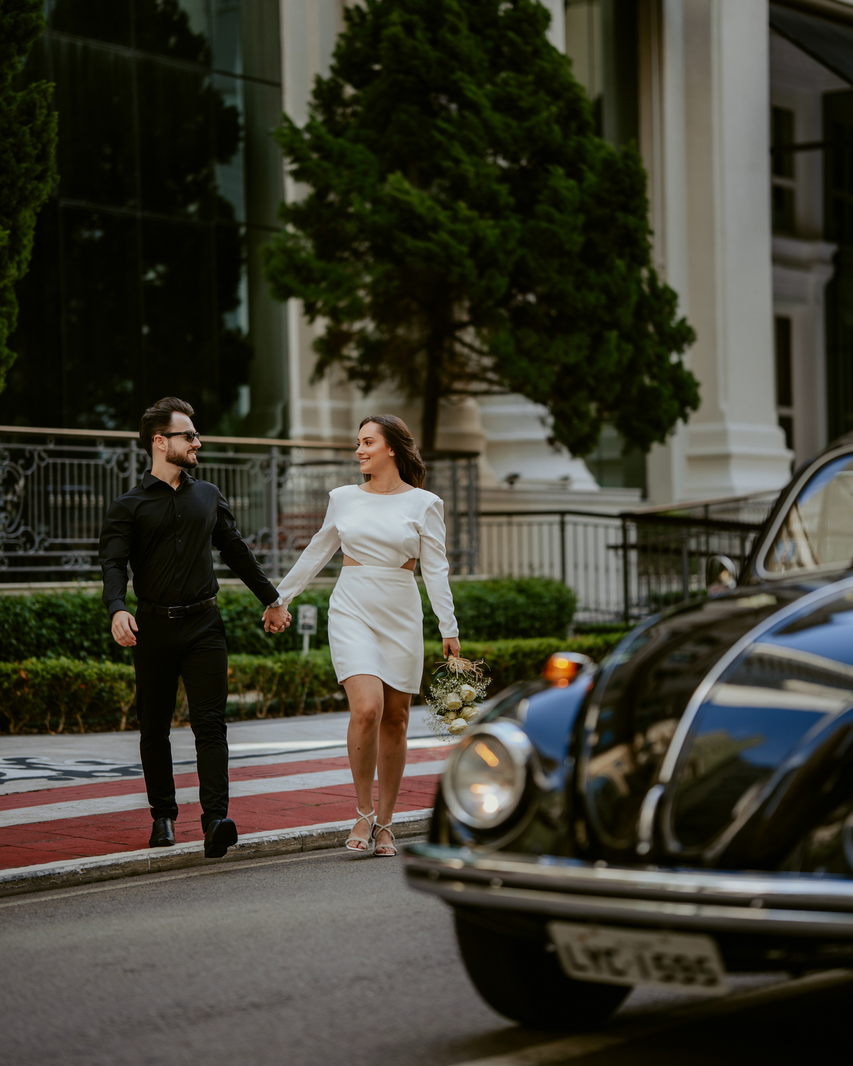 Casal apaixonado em ensaio pré-wedding com arquitetura clássica ao fundo em Balneário Camboriú, composição elegante, roupas sofisticadas preto e branco, fotografia emocional e moderna para casamento