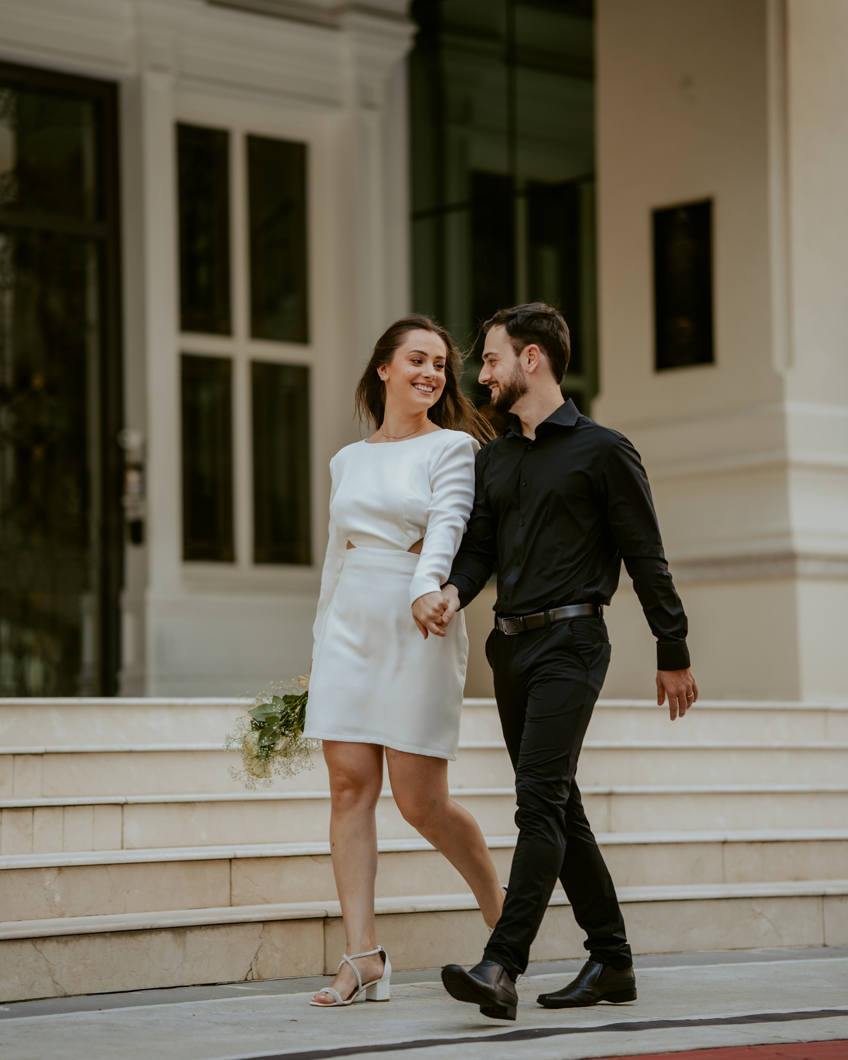 Ensaio pré-wedding na orla de Balneário Camboriú com pôr do sol entre prédios, casal sorrindo com champagne, estilo moderno e divertido, fotografia romântica com luz dourada e cenário urbano contemporâneo