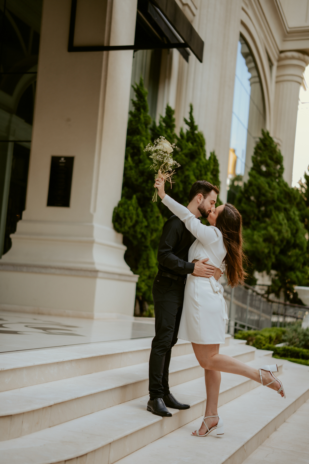 Ensaio pré-wedding ao pôr do sol na praia de Balneário Camboriú com skyline urbano ao fundo, casal brindando com champagne, estilo contemporâneo, romântico e espontâneo, fotografia profissional de casamento