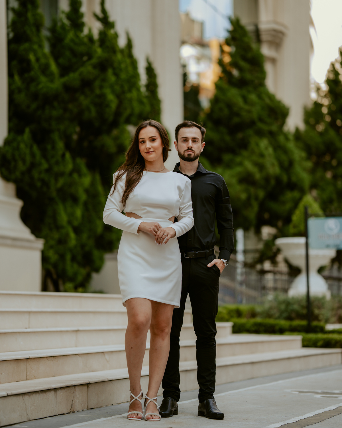 Ensaio pré-wedding na orla de Balneário Camboriú com pôr do sol entre prédios, casal sorrindo com champagne, estilo moderno e divertido, fotografia romântica com luz dourada e cenário urbano contemporâneo