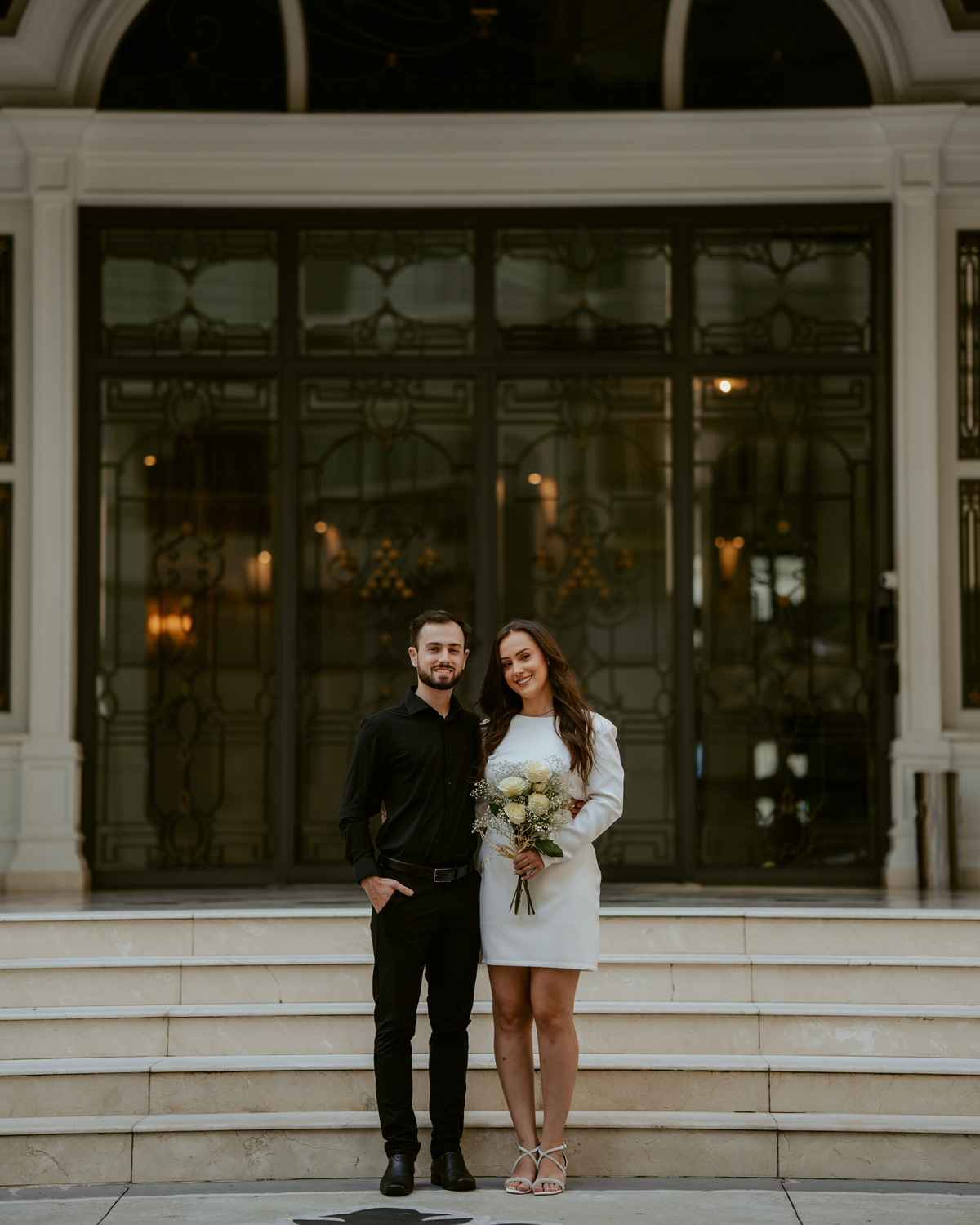 Ensaio pré-wedding na orla de Balneário Camboriú com pôr do sol entre prédios, casal sorrindo com champagne, estilo moderno e divertido, fotografia romântica com luz dourada e cenário urbano contemporâneo