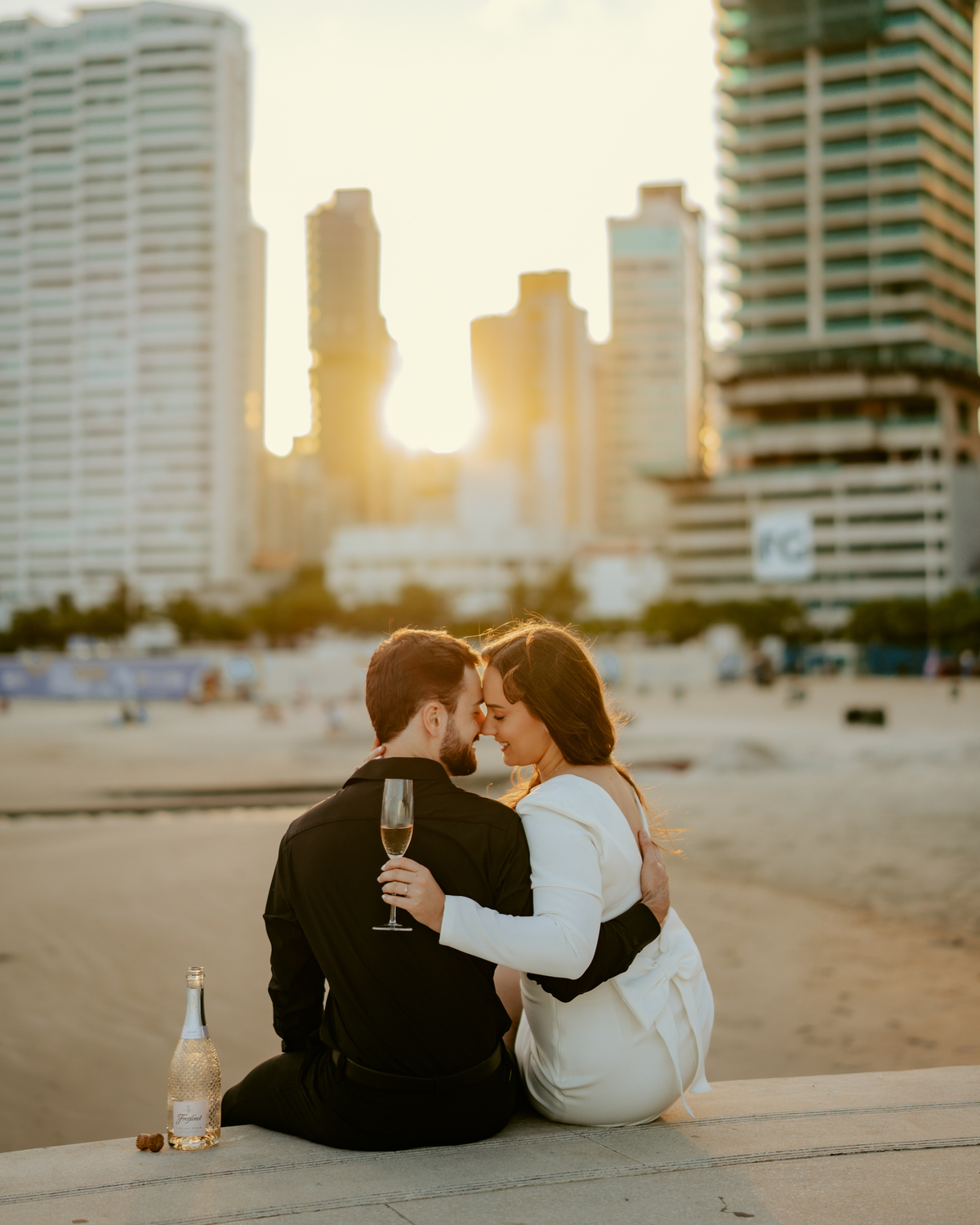 Ensaio pré-wedding no pier da orla de Balneário Camboriú com vista para a roda gigante FG Big Wheel, casal apaixonado em momento espontâneo ao pôr do sol, fotografia romântica moderna com cenário urbano