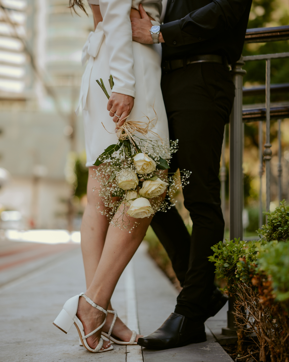 Ensaio pré-wedding moderno em Balneário Camboriú com casal elegante caminhando de mãos dadas em frente a prédio com arquitetura clássica contemporânea, look preto e branco sofisticado, fotografia urbana romântica ao ar livre
