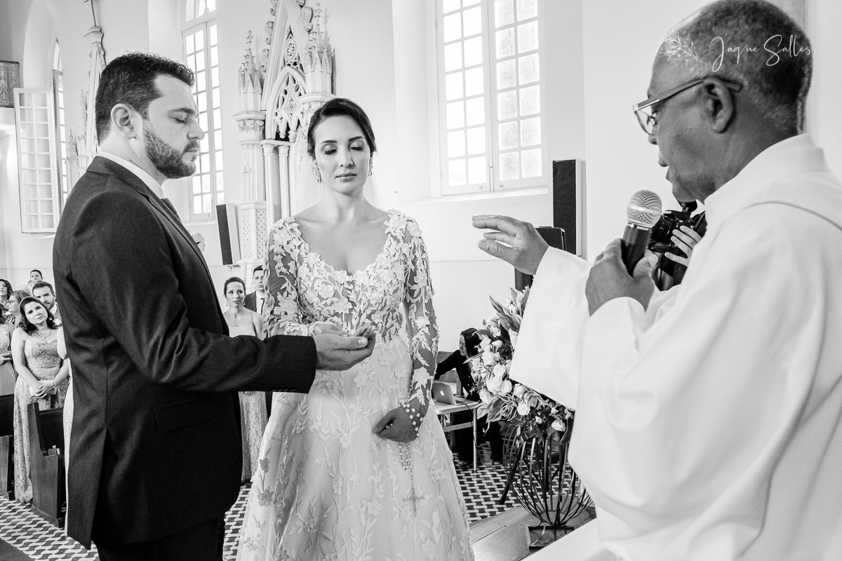 Padre abençoa no altar as alianças dos noivos Priscila e Cadu na Igreja de Santa Thereza D’ávila em Rio das Flores - RJ. Imagens da Fotógrafa de Casamento Jaque Salles Fotografia