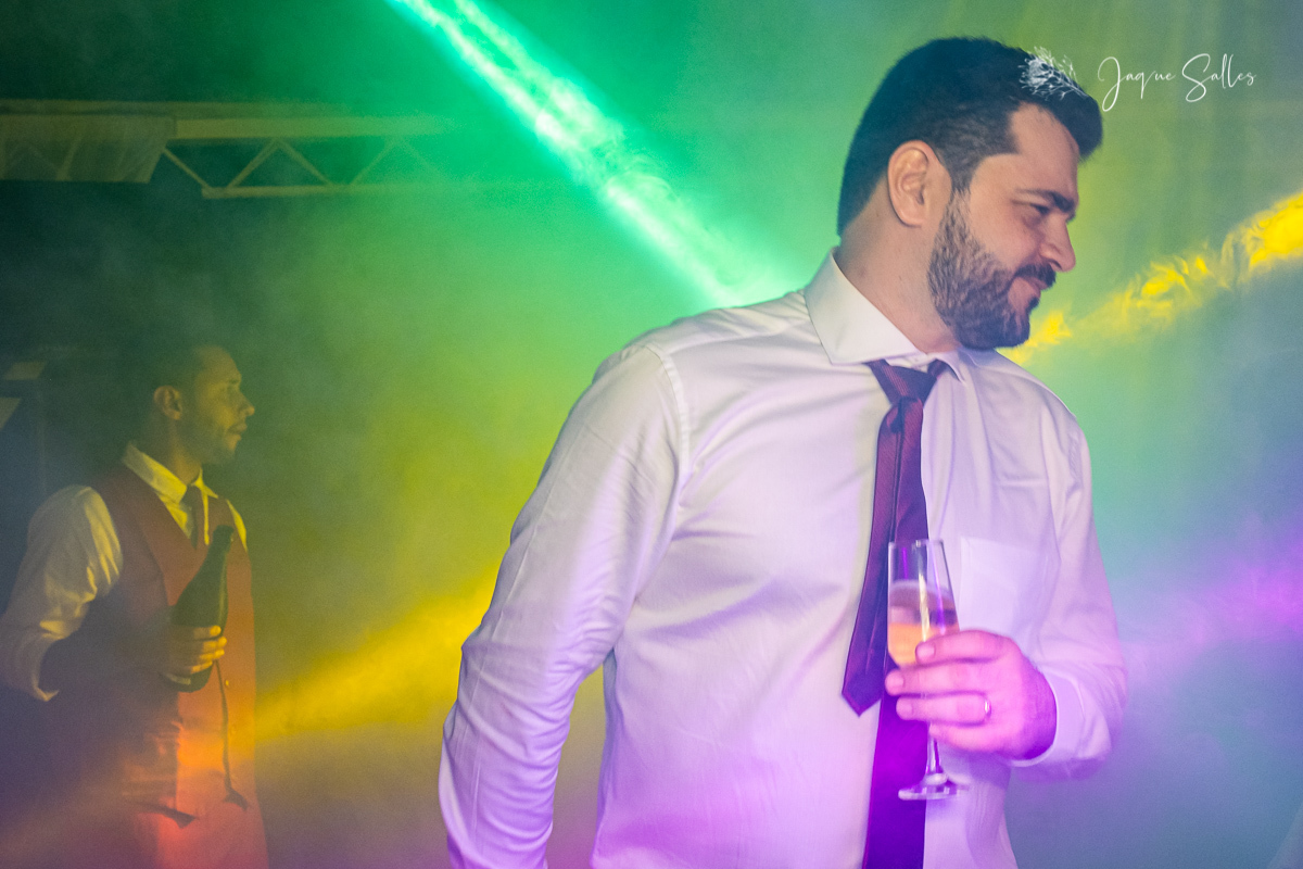 Foto do Noivo Cadu segurando uma taça de espumante em sua Festa de Casamento. Fotografia da Fotógrafa de Casamento Jaque Salles Fotografia