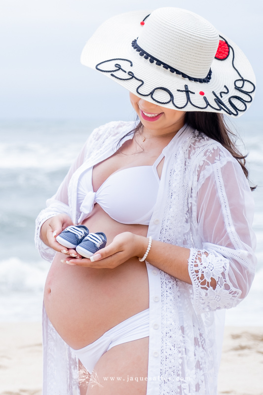 Ensaio Gestante da Letícia no Rio de Janeiro, RJ. O Ensaio Fotográfico aconteceu na Prainha região do Recreio dos Bandeirantes e teve a Fotografia de Jaque Salles. Na Foto a Gestante aparece sorrindo e olhando para o sapatinho do Bebê.