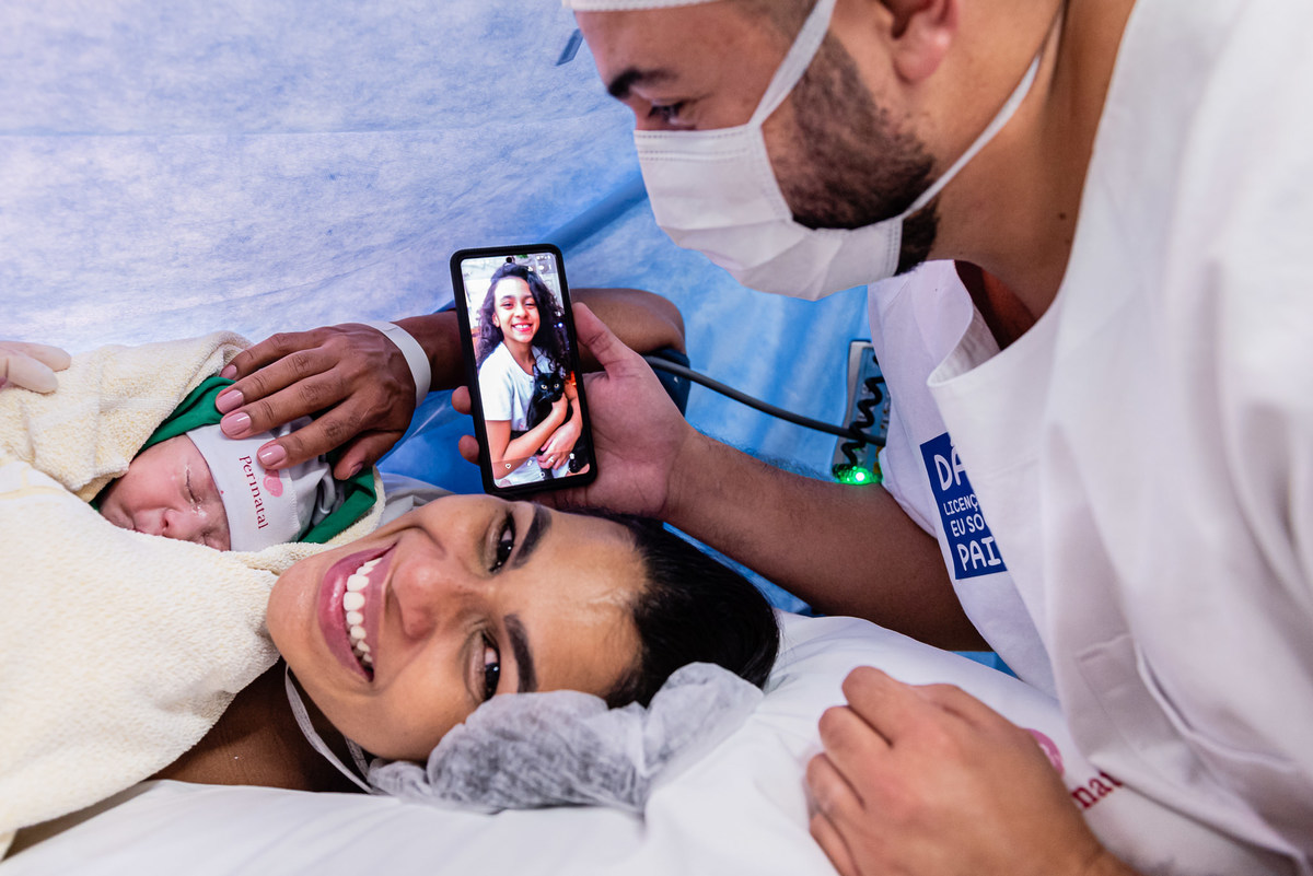 Imagem do recém nascido Gustavo no colo da mãe, do pai  e com imagem da irmã ao celular. Gustavo nasceu na  Maternidade Perinatal da Barra da Tijuca. Imagens da fotógrafa de casamento e famílias Jaque Salles 