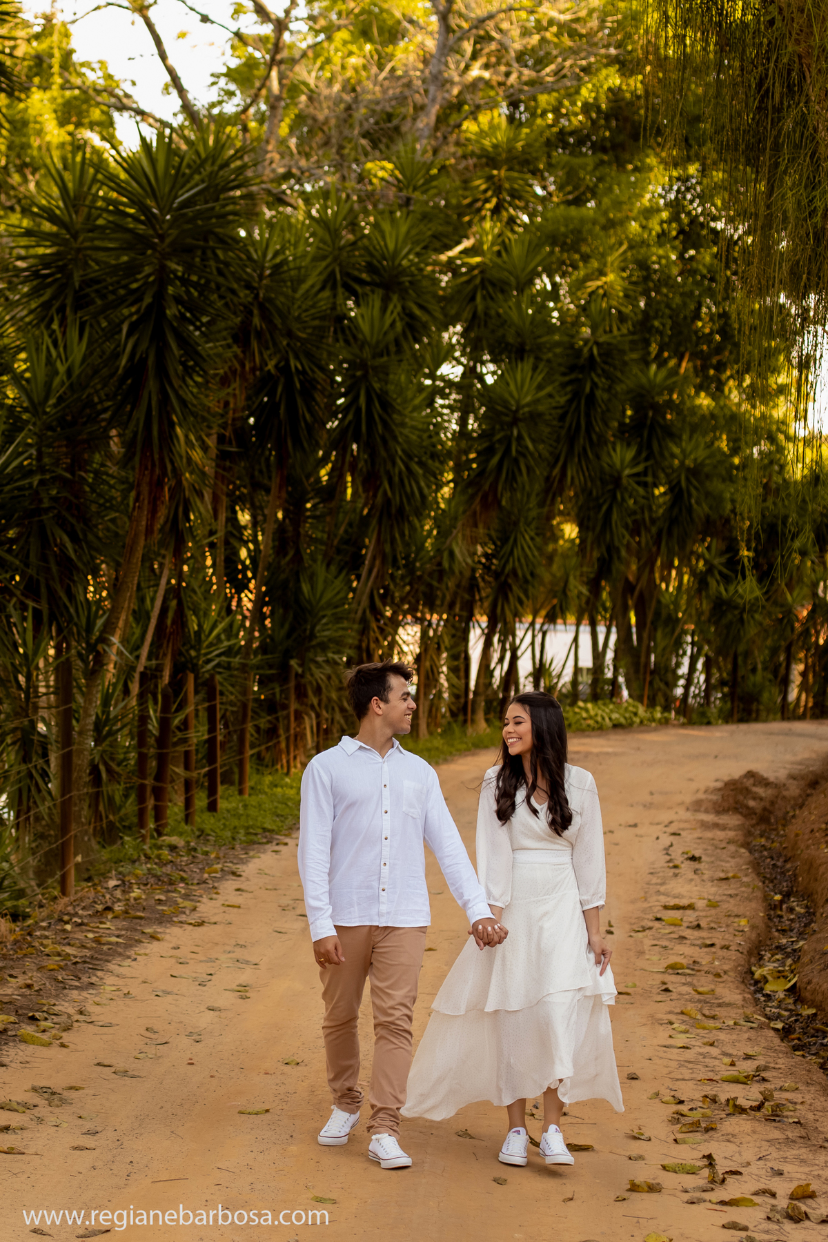Ensaio casal estradinha rural vestido branco camisa branca e calca marrom allstar branco caminhando