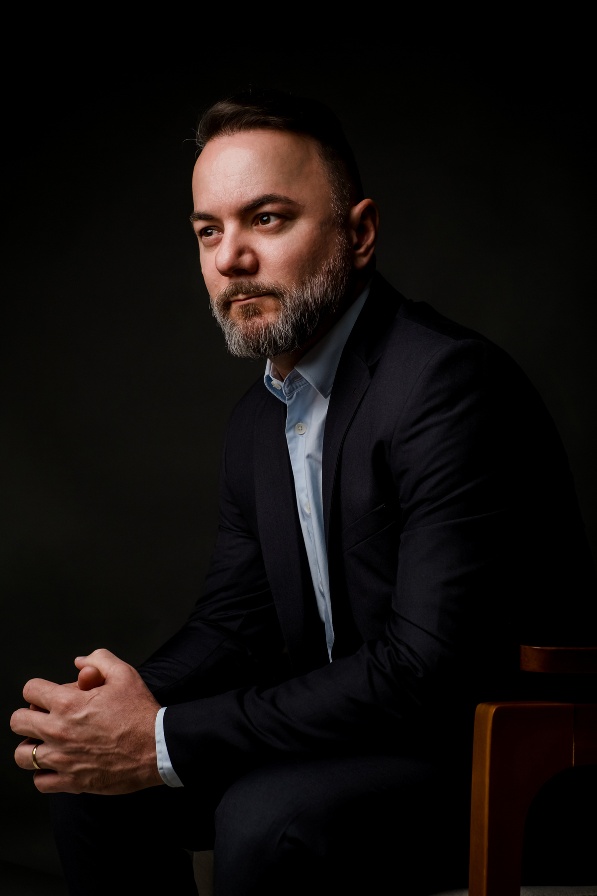 Homem em postura executiva ajustando o terno escuro, camisa azul, transmitindo elegância e prontidão contra fundo preto.