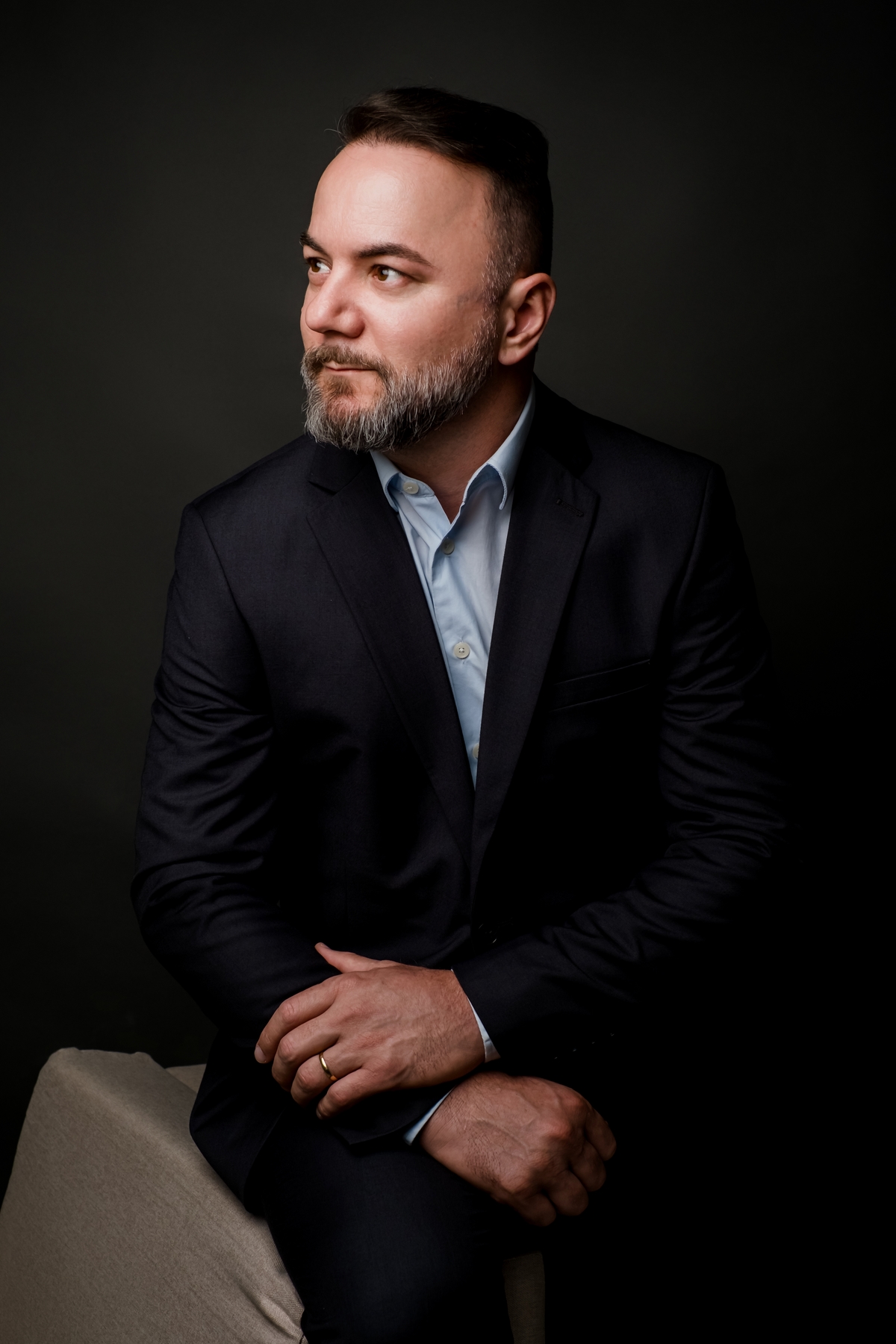 Executivo sentado olhando para o lado, postura pensativa com braços cruzados, fundo escuro sofisticado.
