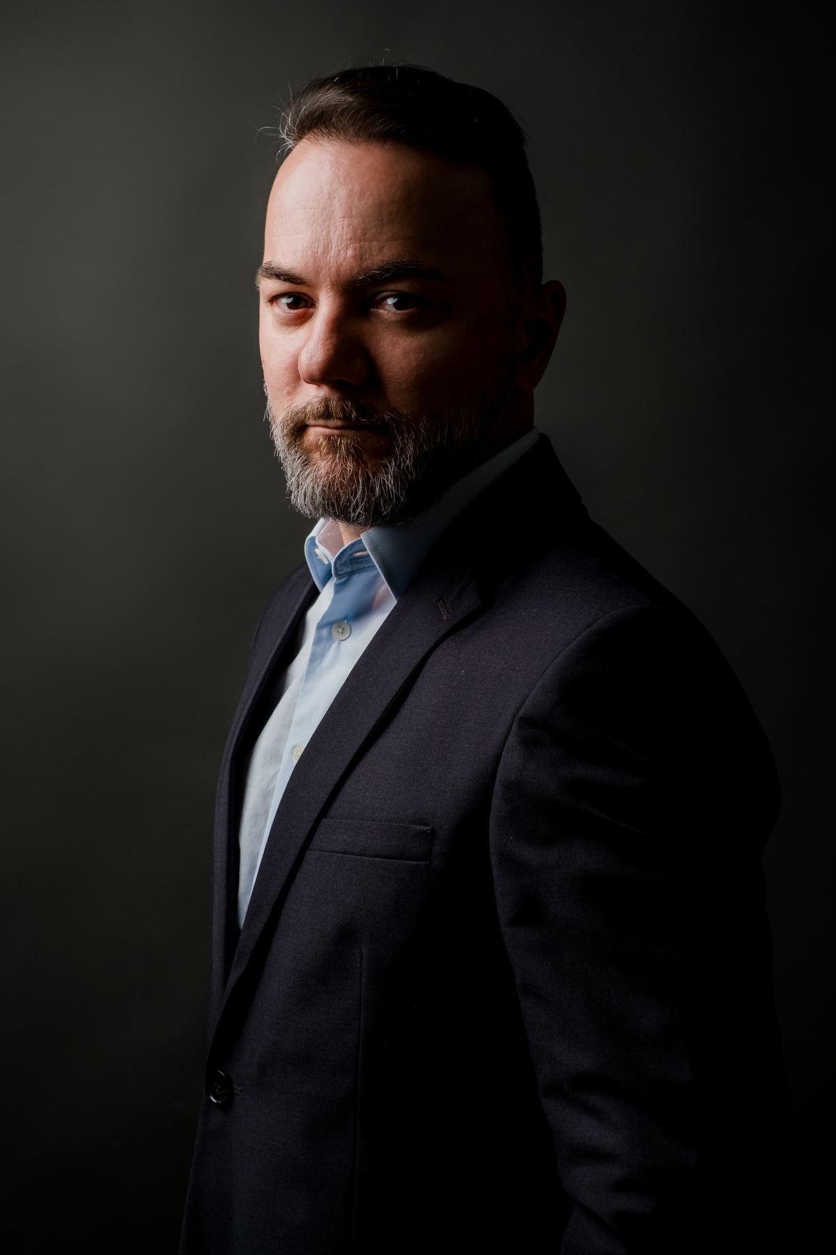 Retrato corporativo masculino em meio perfil com olhar por cima do ombro, luz contrastante e terno escuro.