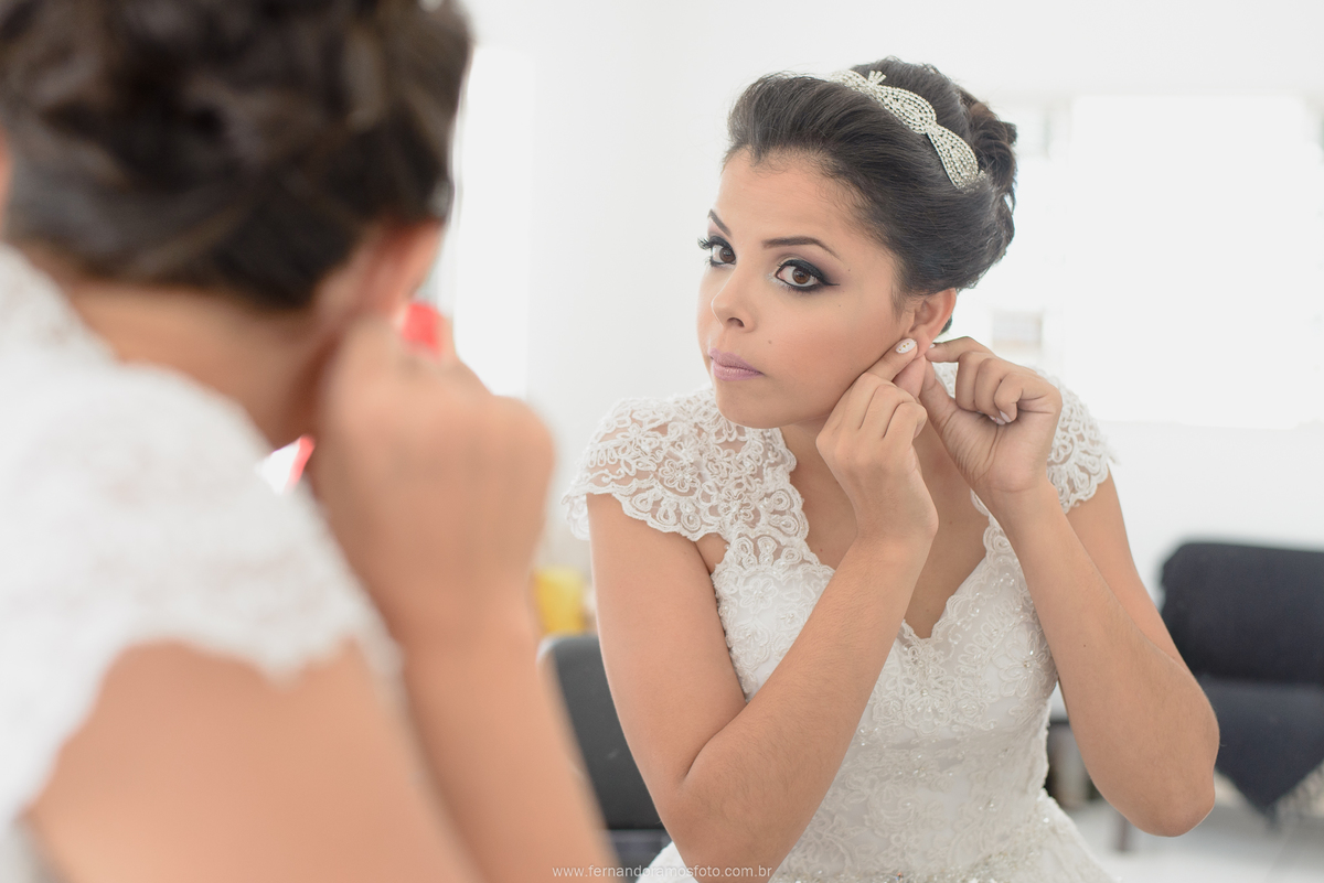 FOTO DE NOIVA COLOCANDO O BRINCO DURANTE MAKING OF NO SALÃO DE BELEZA CAROL FRANÇA AMKE UP
