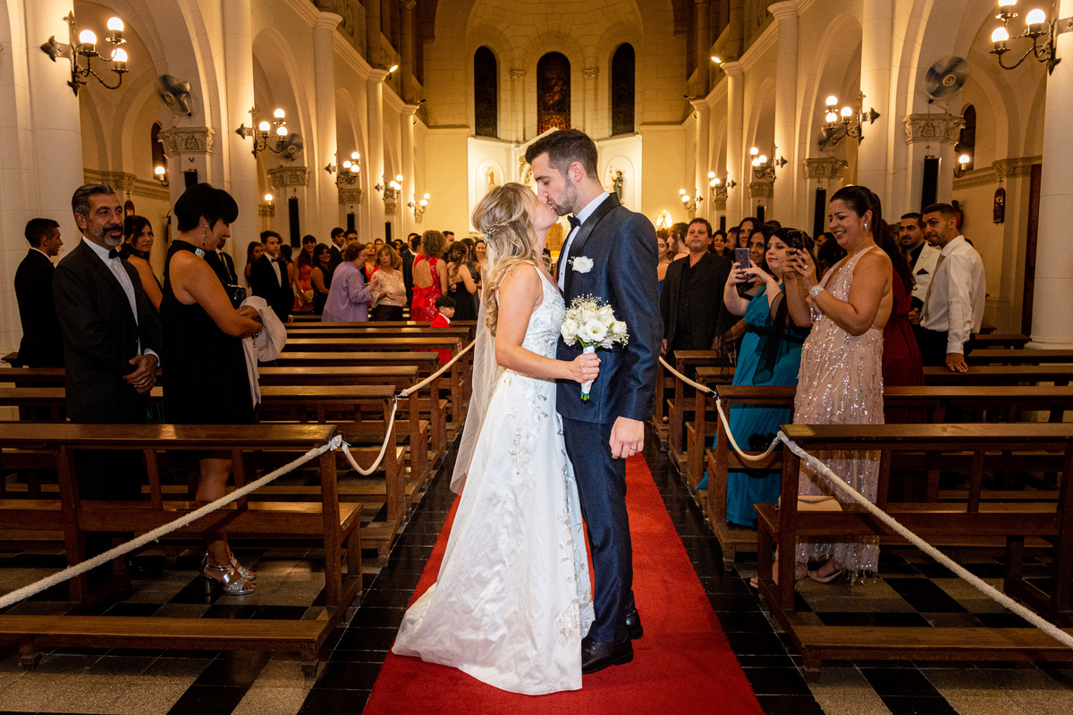 Beso al final de la alfombra roja de la iglesia Santiago Apóstol. Marcos Pasquare fotógrafo de bodas. Nuñez, Caba.