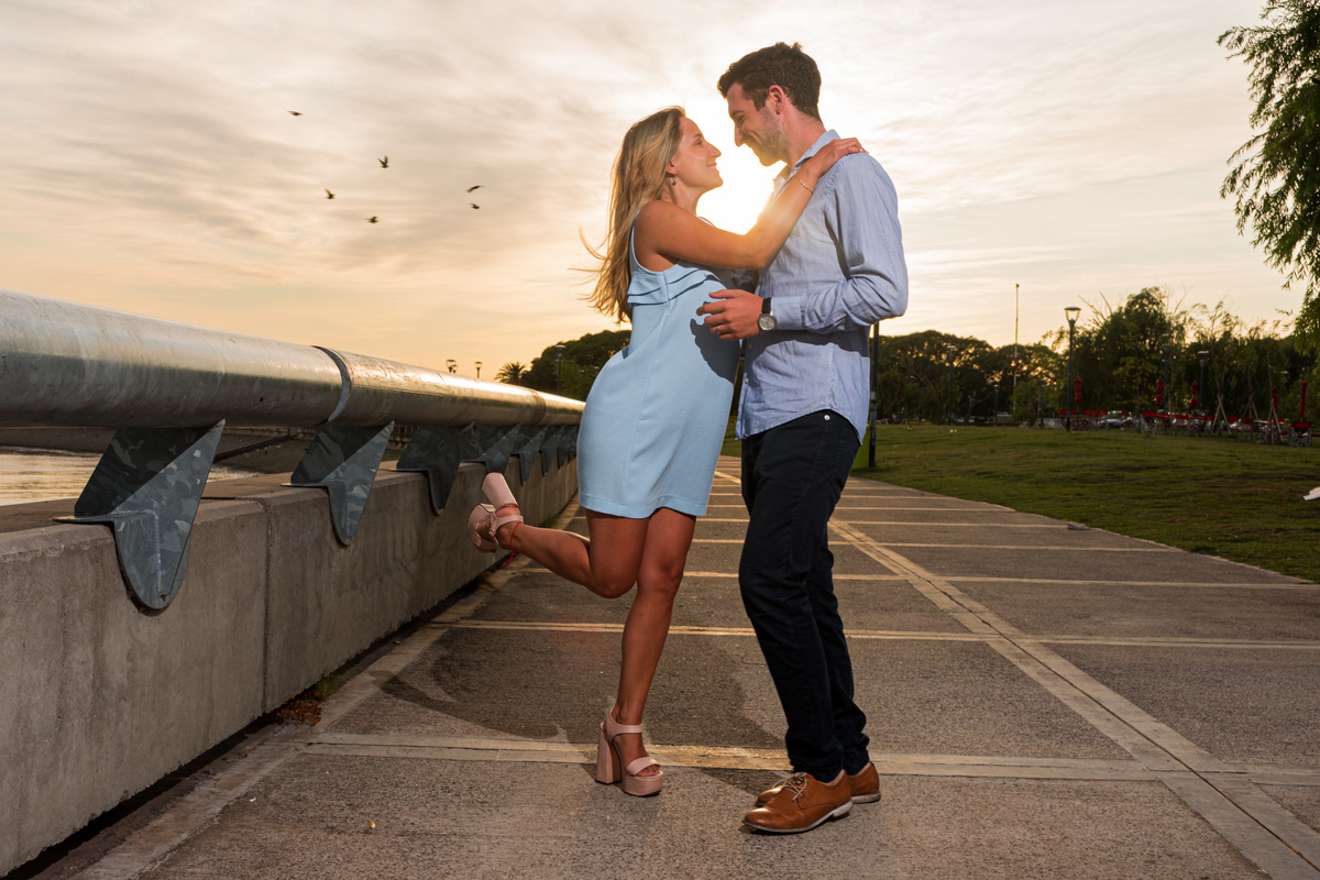 Sesión pre boda. Novia levanta la pierna y se miran, el sol brilla detras de ellos. Las aves vuelan. Costanera Norte, CABA. Marcos Pasquare fotógrafo de bodas