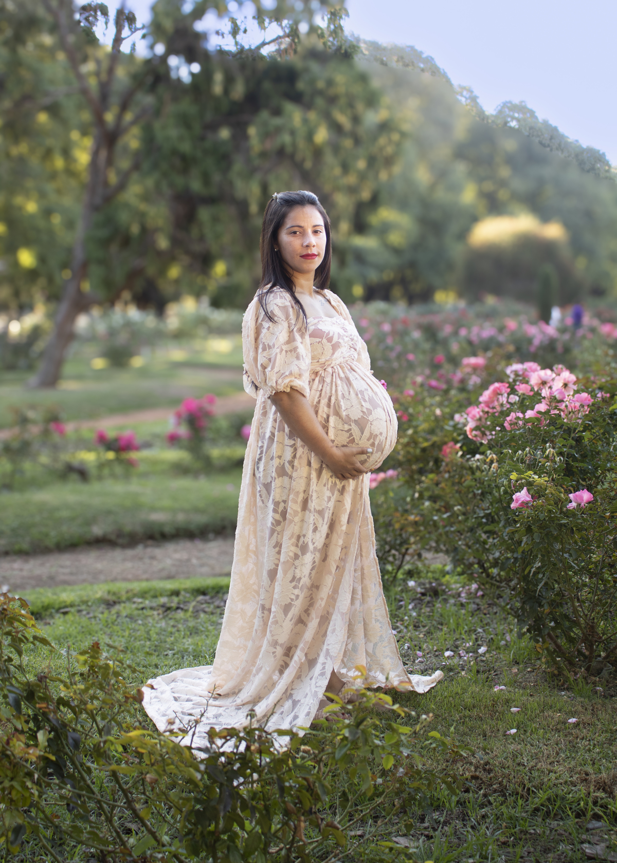 embarazada en jardín de rosas, de perfil mirando al frente, vestido romántico
